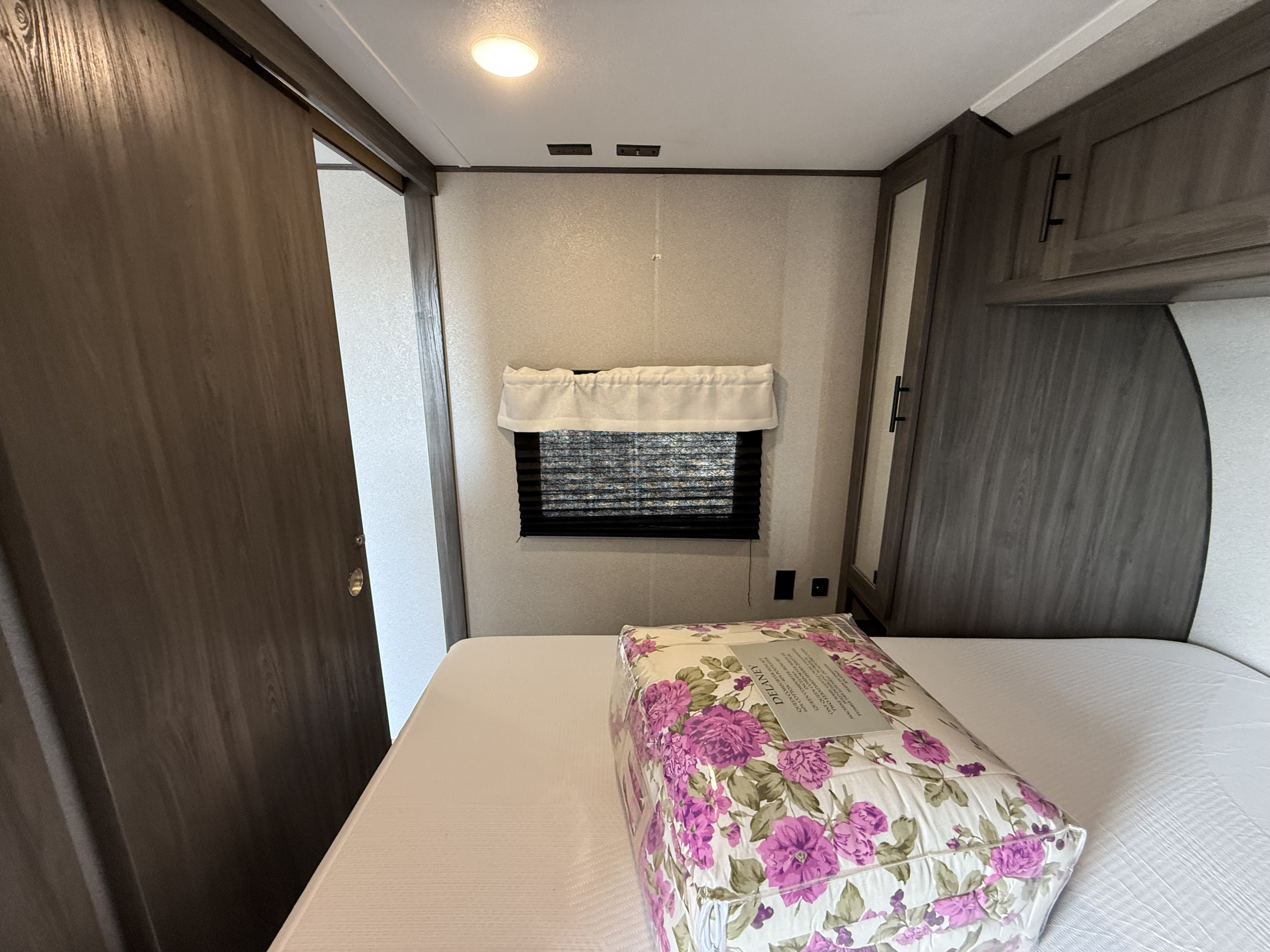 This RV rental bedroom features a new floral comforter on the bed, a window with blinds, and a wood-look sliding door.. Forest River Shasta 2021
