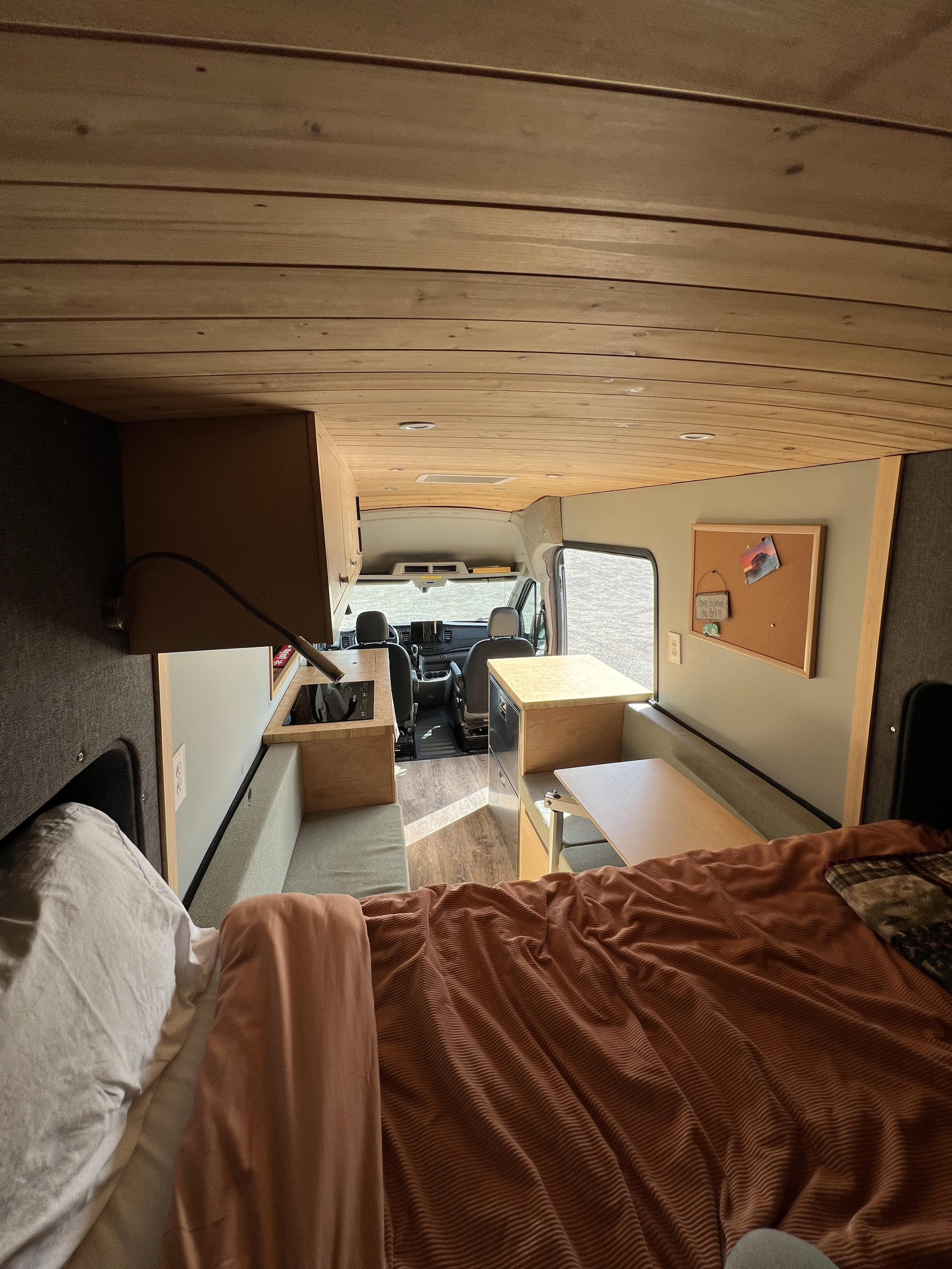 Explore this custom RV rental, featuring a comfortable bed, functional kitchen, and dining/lounge area, perfect for travel.. Ford Transit 2022