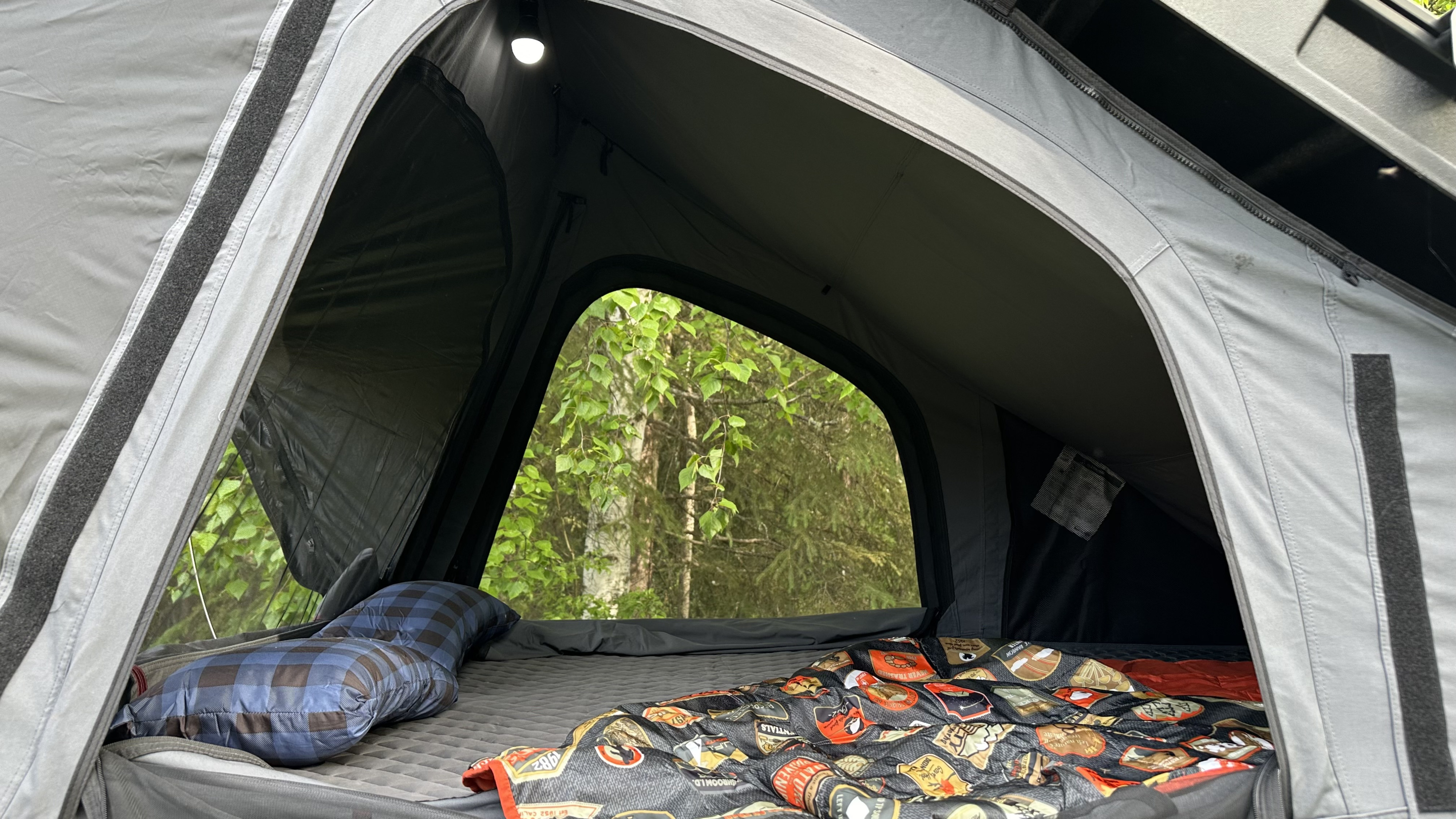 Cozy RV rental rooftop tent interior: a comfy bed, pillow, and nature views through the open archway. A small light is above.. 1C6HJTAGXPL573890 Jeep Gladiator 2023