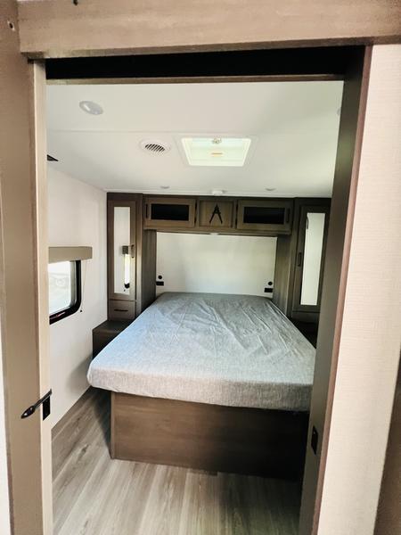 Spacious RV rental interior featuring a comfortable bedroom with a full-size bed, ample overhead storage, and side tables.. Grand Design Transcend 245RLT 2025