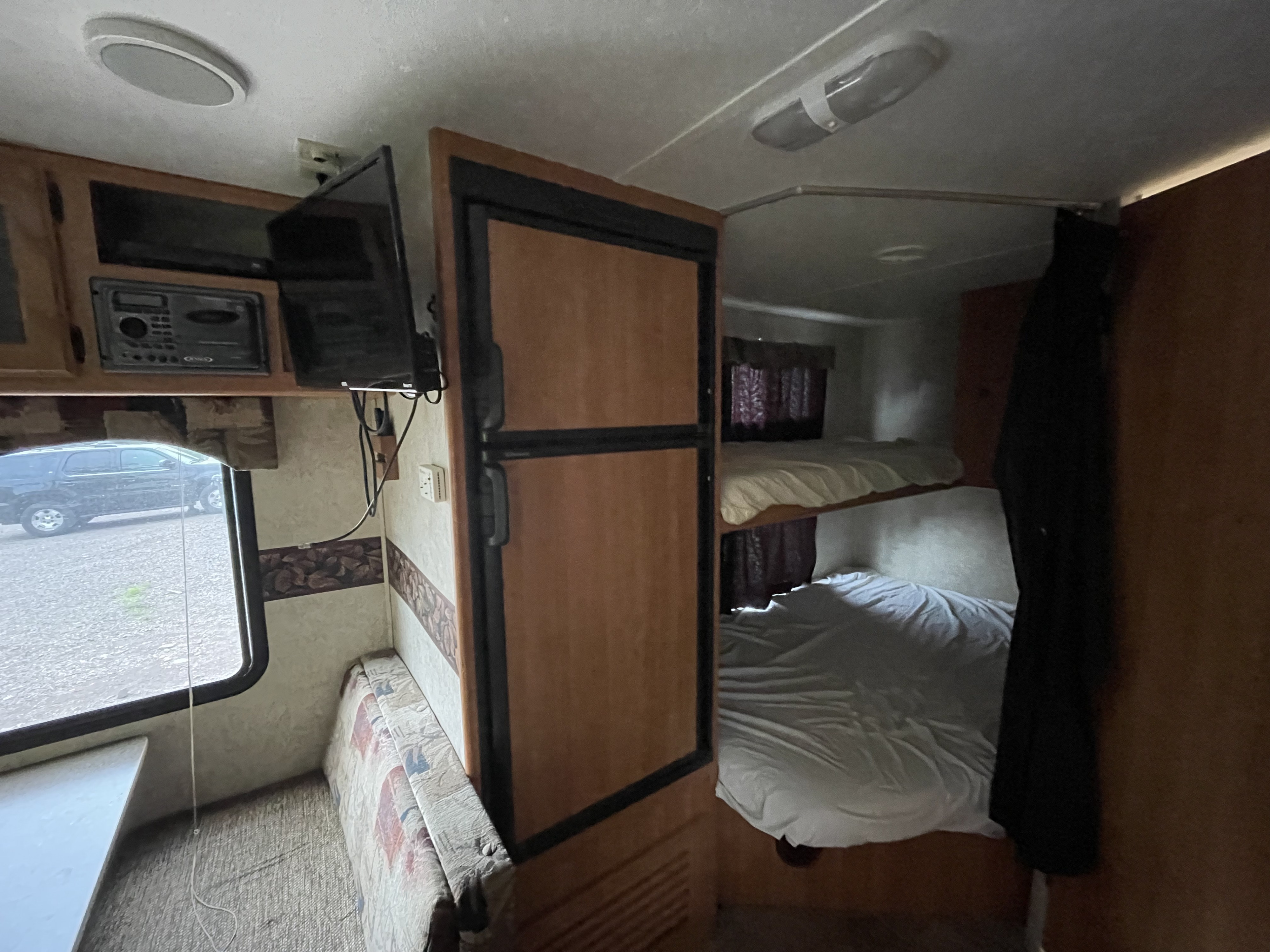 Interior of an RV rental: includes bunk beds, an entertainment system (TV, stereo), refrigerator, and a window view.. Keystone RV Passport 2008