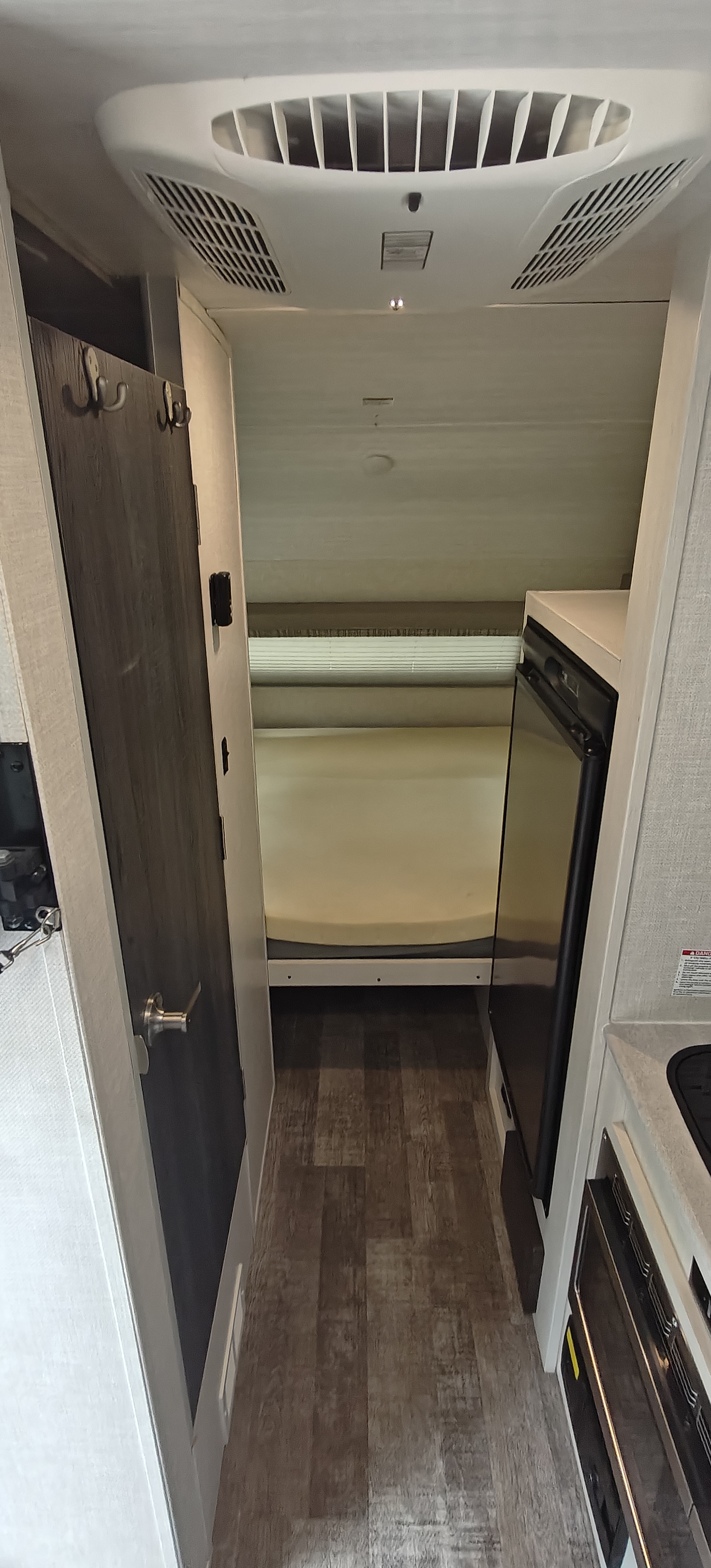 Looking down a small RV rental hallway, revealing a bed, fridge, kitchen, and ceiling AC unit.. Forest River R-Pod 2023