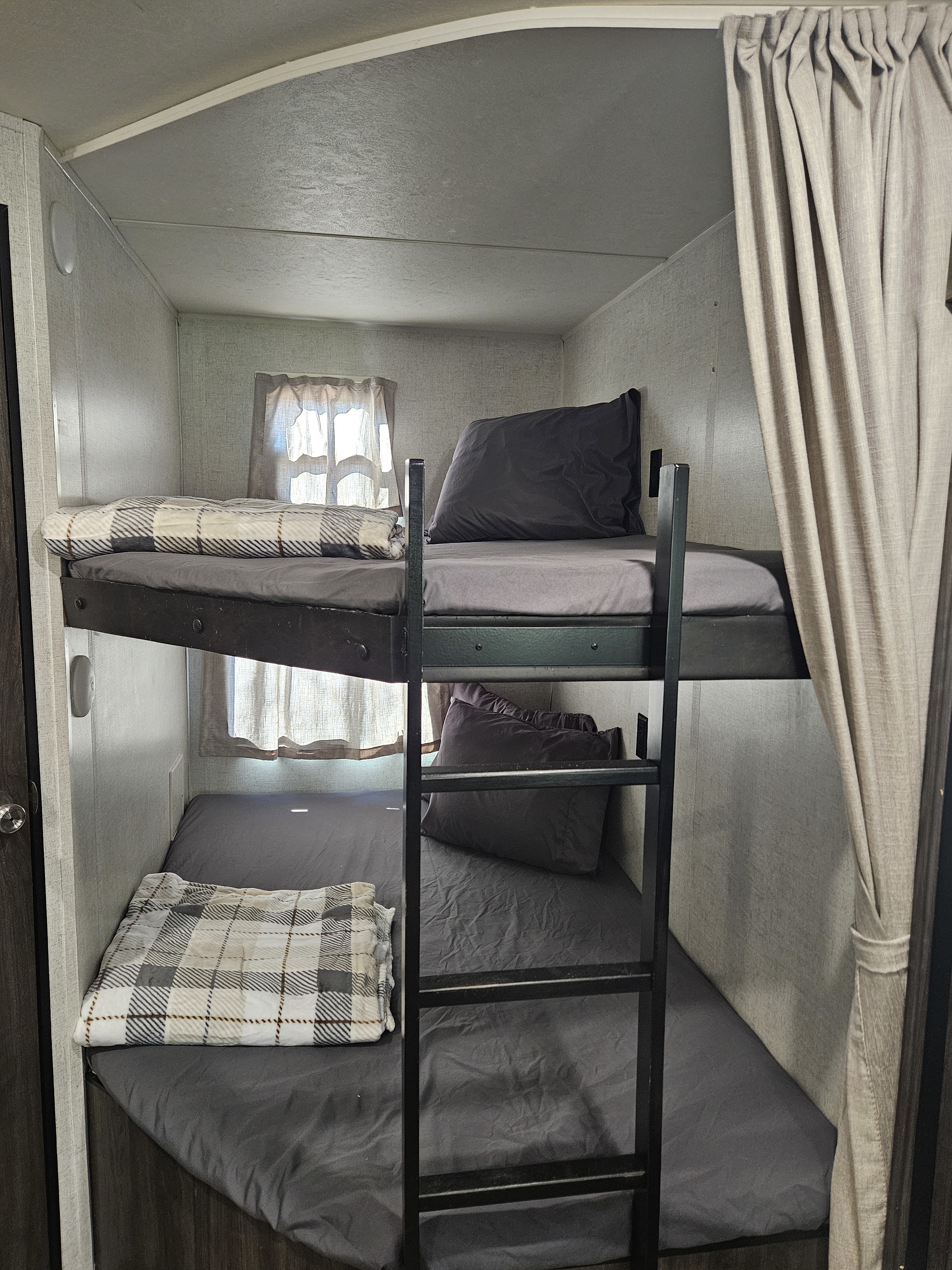 Cozy bunk beds with grey sheets and a plaid blanket inside an RV rental, perfect for family adventures.. Starcraft Autumn Ridge 2020
