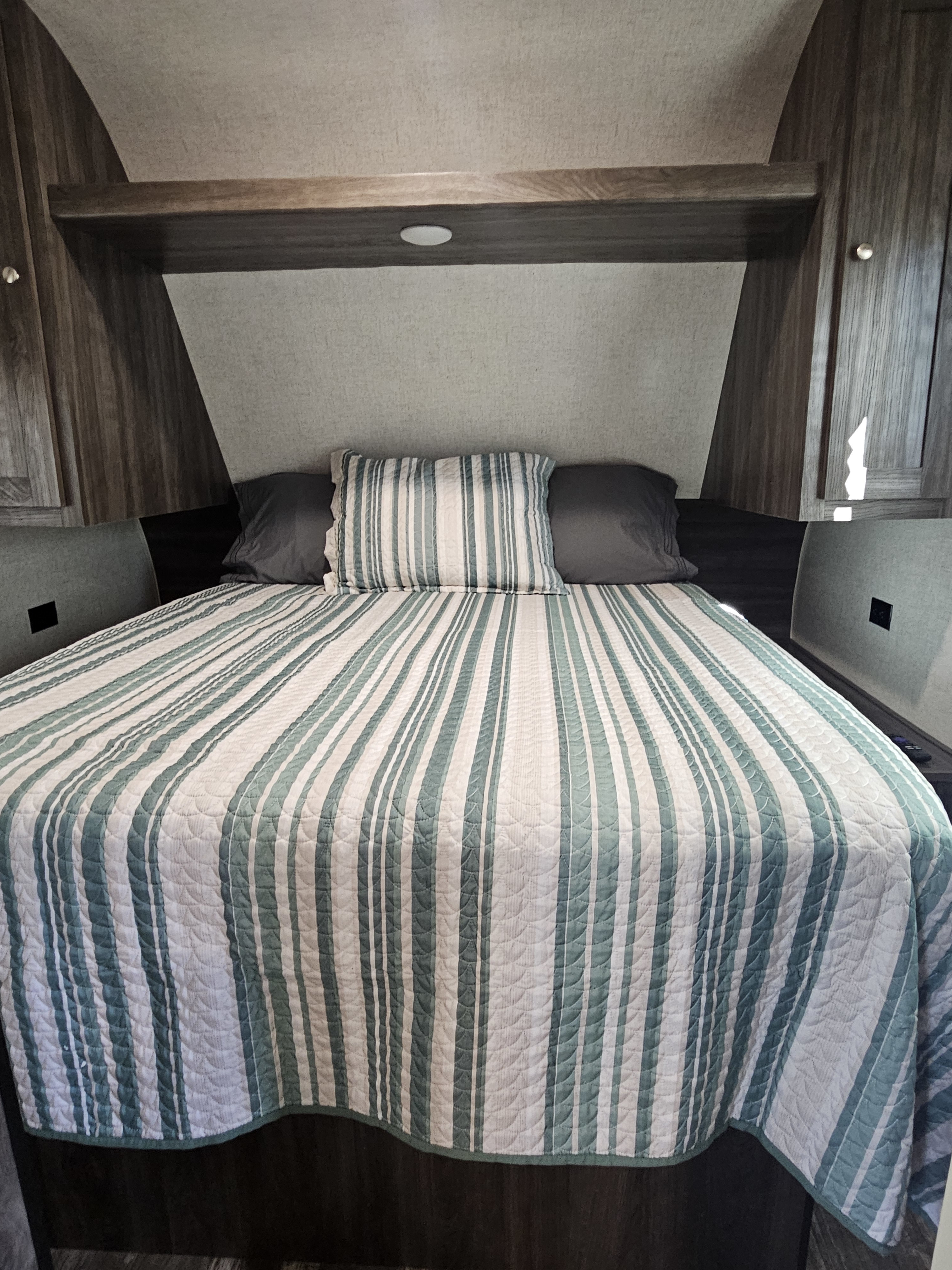Cozy RV rental bedroom featuring a bed with a white and green striped quilt and dark pillows, set within a wood-paneled interior.. Starcraft Autumn Ridge 2020