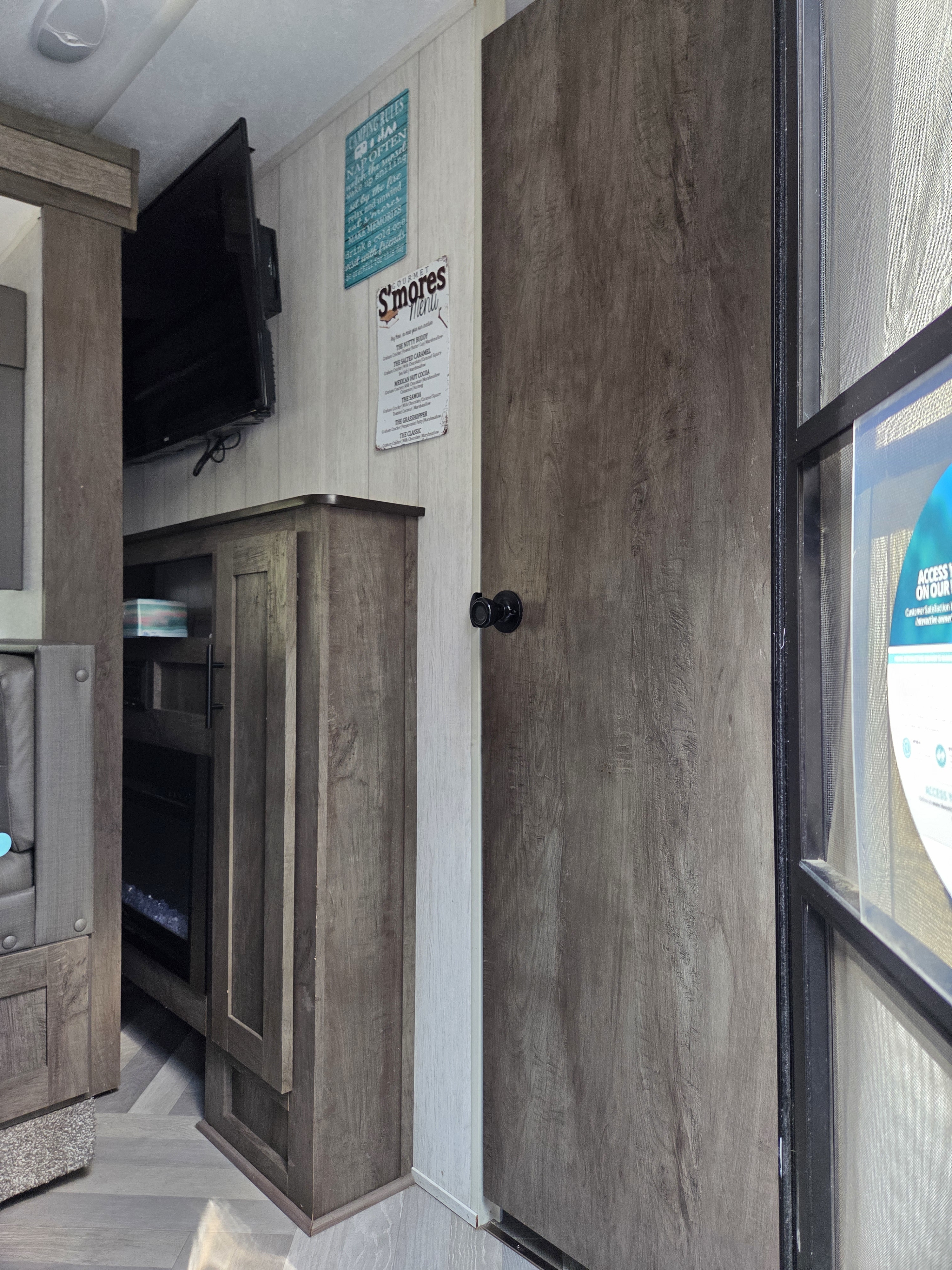 Cozy RV rental interior featuring a TV, wood cabinets, and fun "Camping Rules" & "S'mores Menu" wall decor.. Forest River Wildwood X-Lite 2020