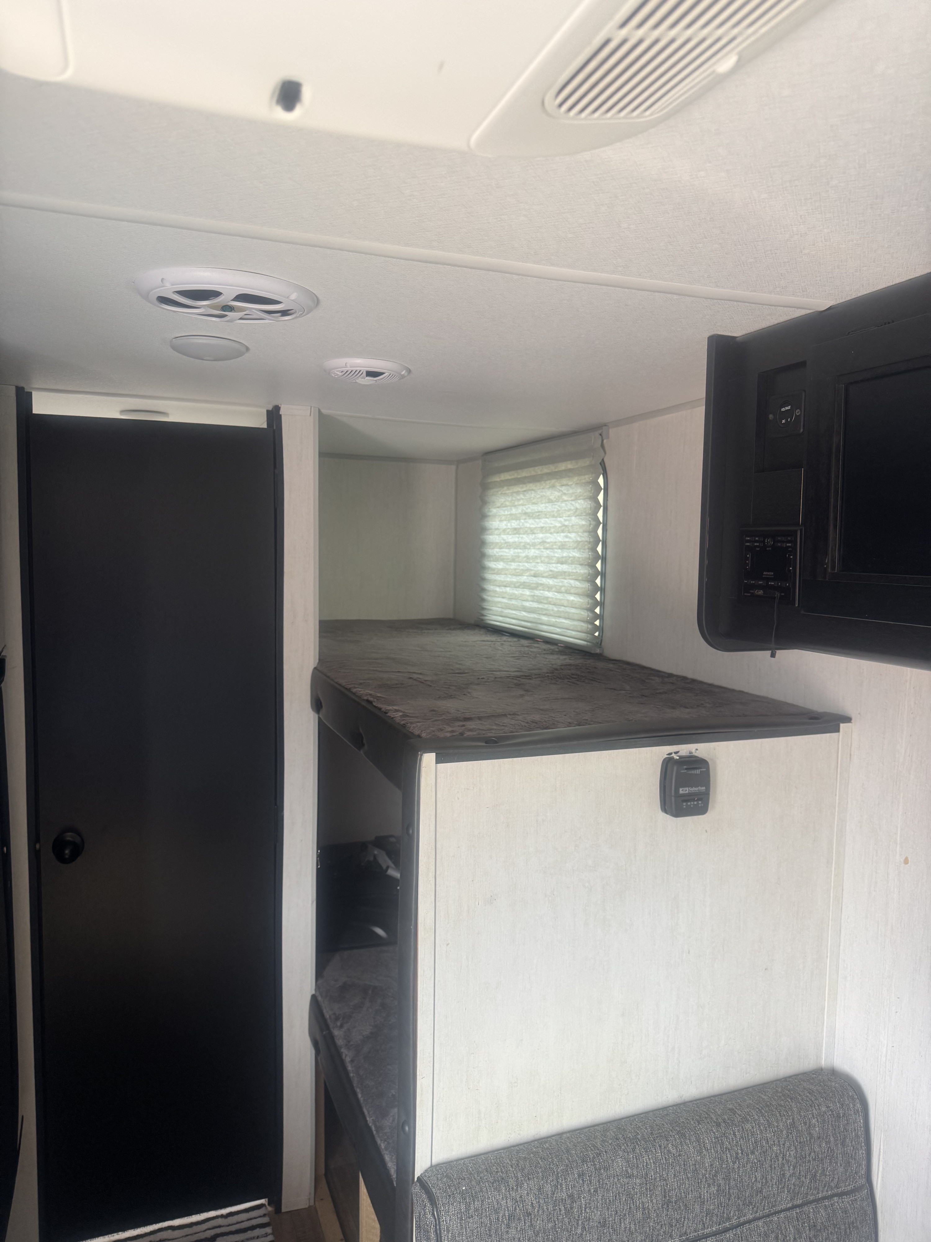 An **rv rental** interior, showcasing bunk beds, a wall-mounted TV, and a black door, optimized for compact living.. Forest River Cherokee Wolf Pup 2022