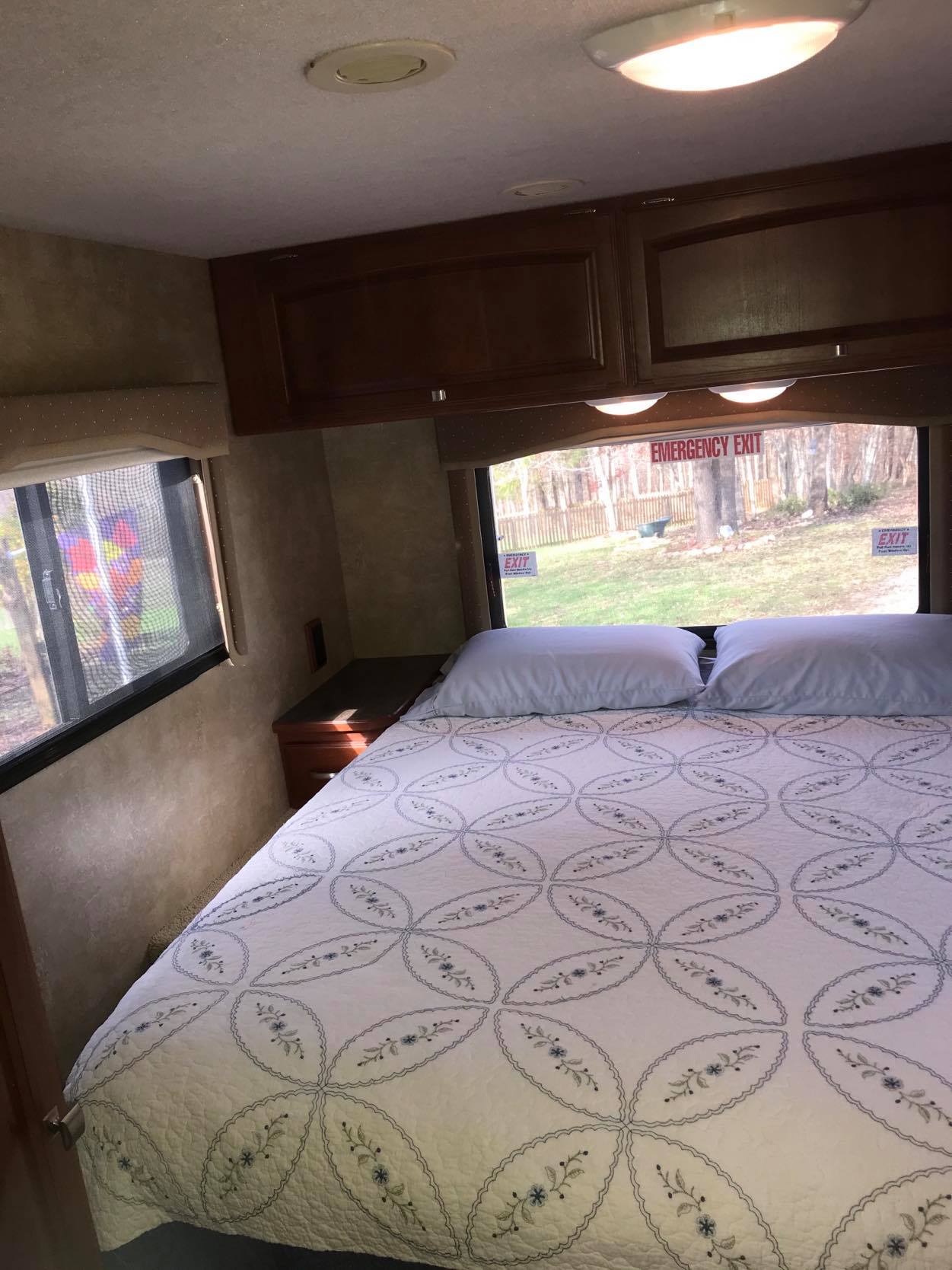 Cozy RV rental bedroom with a comfortable bed, ample storage, and emergency exits, perfect for your next mobile adventure.. Winnebago Chalet 2015