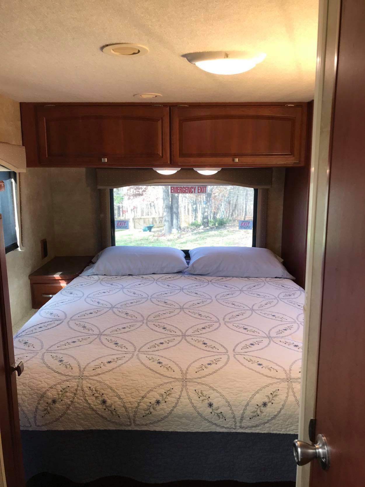 Interior of a clean RV rental bedroom. Features a neatly made queen bed, ample overhead storage, and large windows.. Winnebago Chalet 2015