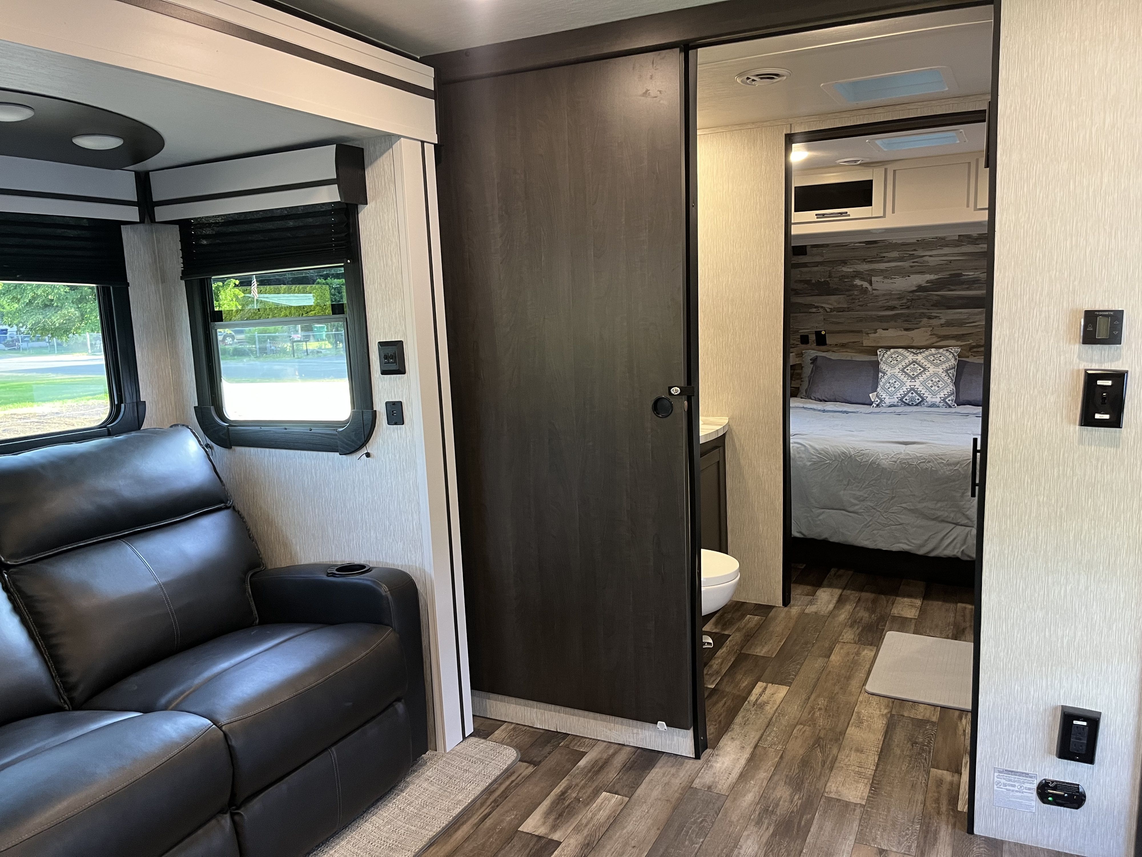 Modern RV rental interior: a comfy living area with a sofa leads to a private bedroom via a sliding door and bathroom access.. Crossroads RV Cruiser Aire 2022