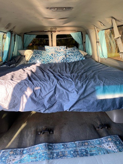 Comfortable RV rental van sleeping area. Features a large bed with blue linens & privacy curtains.. Ford E350 Box Van 2003