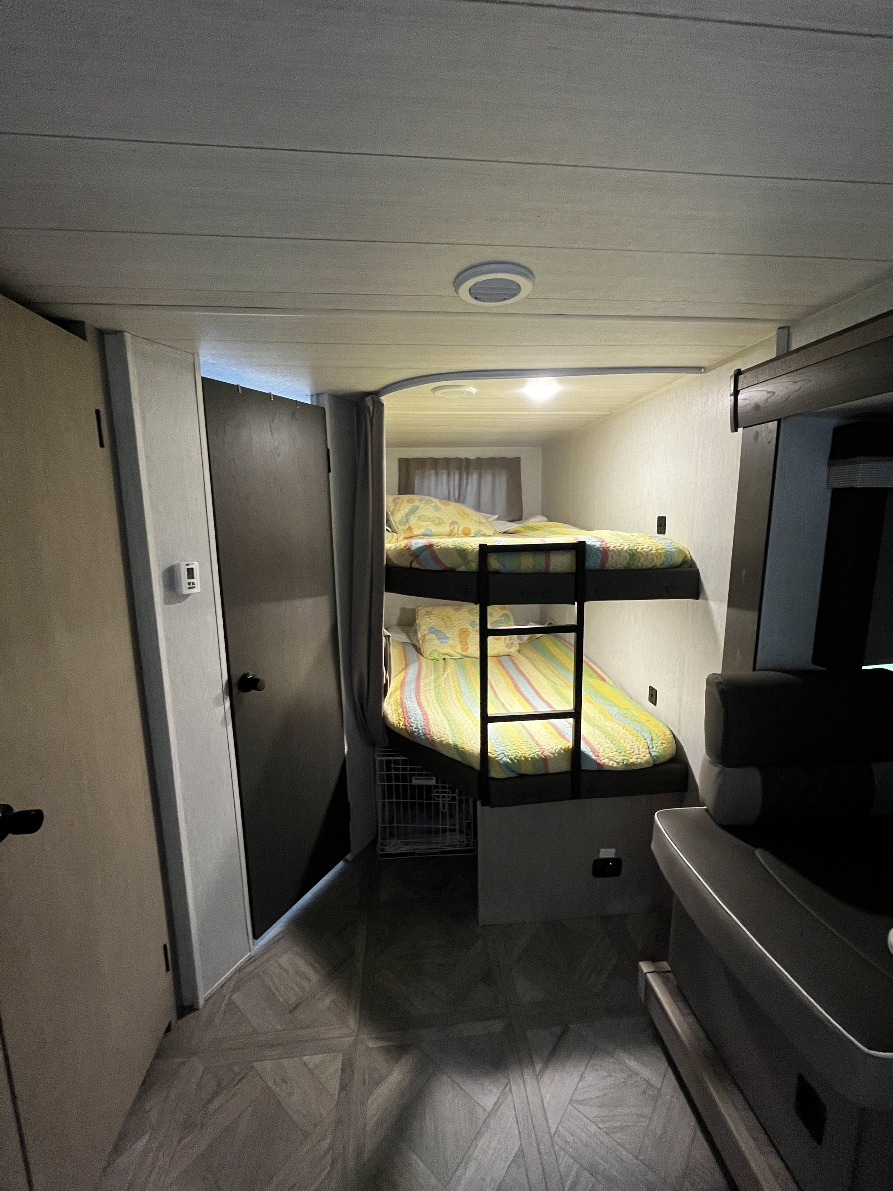 This RV rental features a cozy interior with bunk beds, colorful bedding, a pet crate, and a small seating area.. Forest River Wildwood X-Lite Platinum 2024