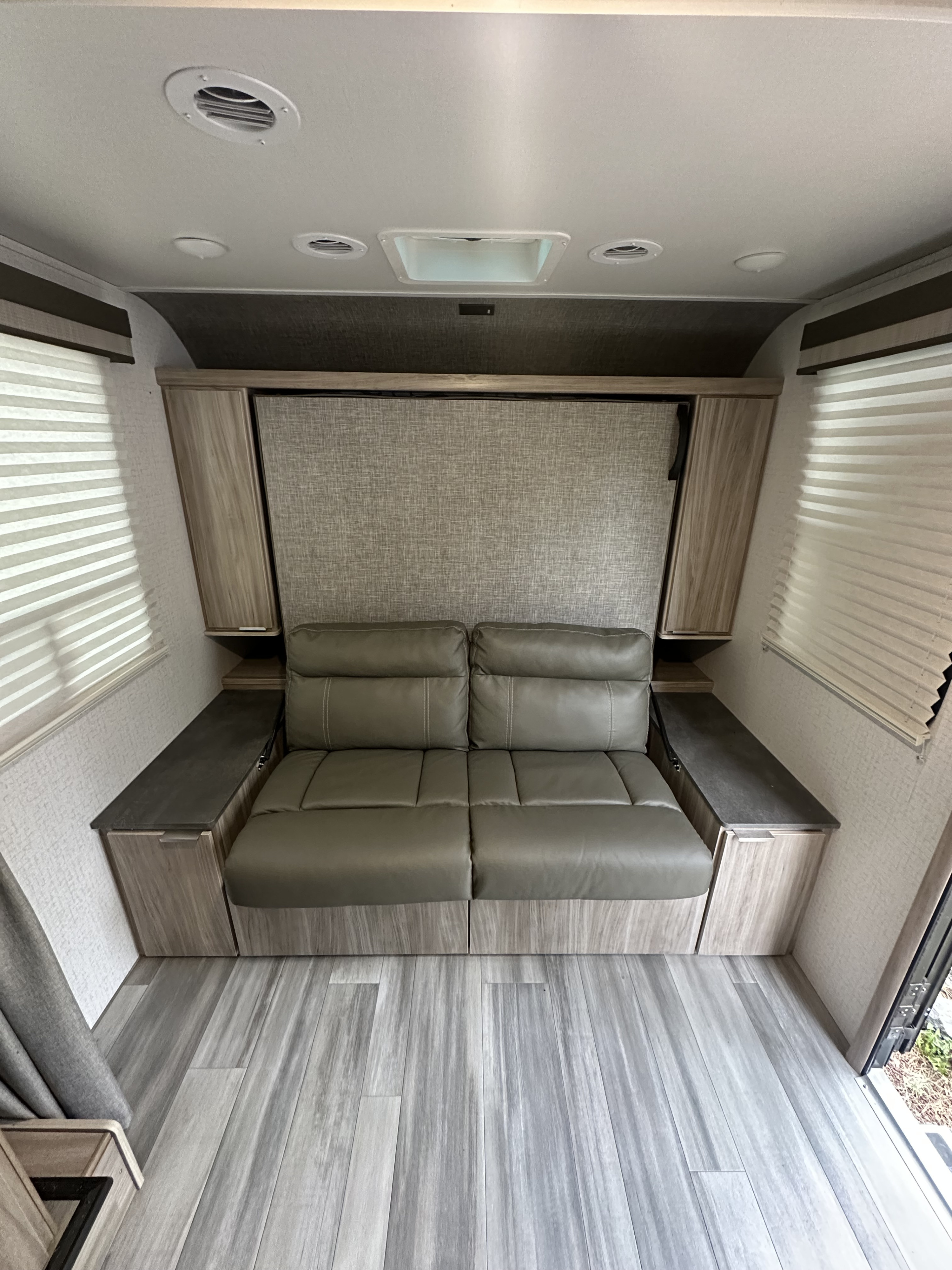 Spacious rv rental interior showing a cozy gray sofa, convertible bed, side storage, and wood-look flooring.. Winnebago Minnie Winnie 2021