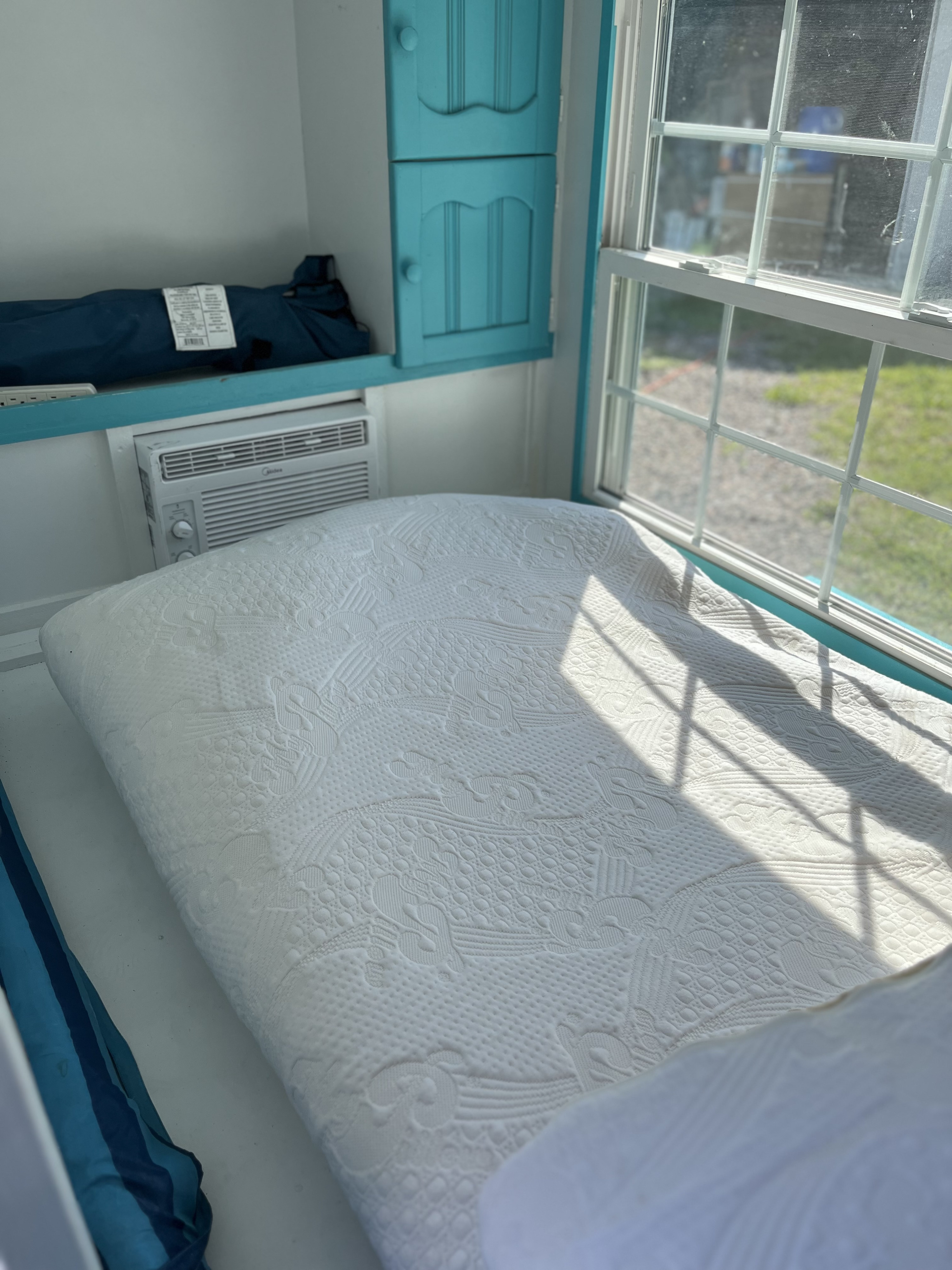 RV rental: Compact interior features a comfy bed, window with sun, Midea AC unit, and turquoise cabinets.. YNGQ Box 2017