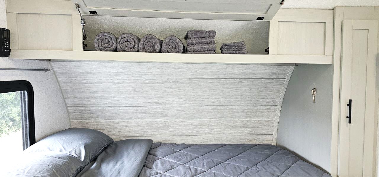 Relax in this RV rental bedroom. Features gray bedding, a shiplap headboard, and organized overhead storage with fresh towels.. Forest River Wildwood FSX 2022