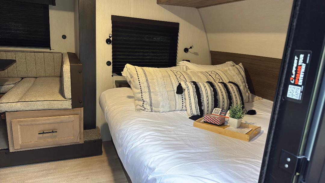 Cozy RV rental interior featuring a comfortable bed with decorative pillows, a dining booth, and dark window blinds.. Forest River Cherokee Wolf Pup 2025