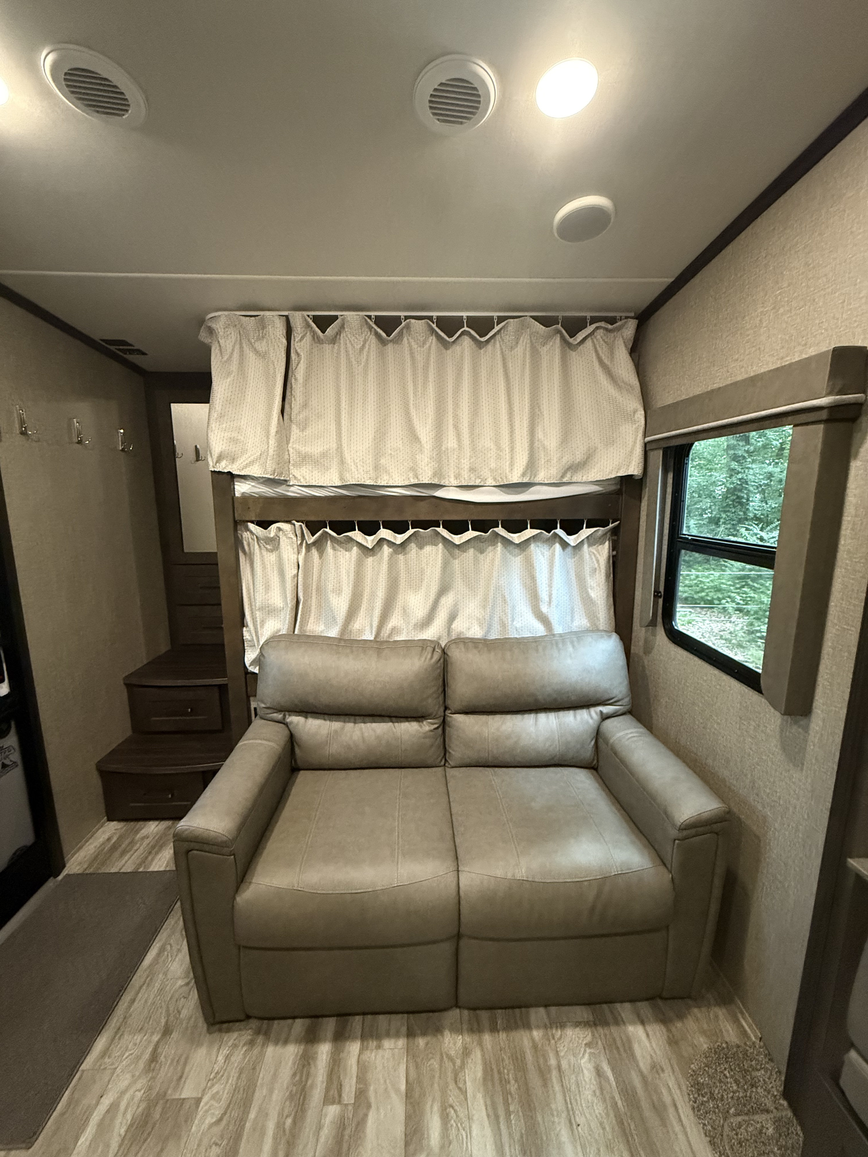 Cozy RV rental interior with a light brown sofa facing functional bunk beds, steps, and a window.. Grand Design Reflection 2020