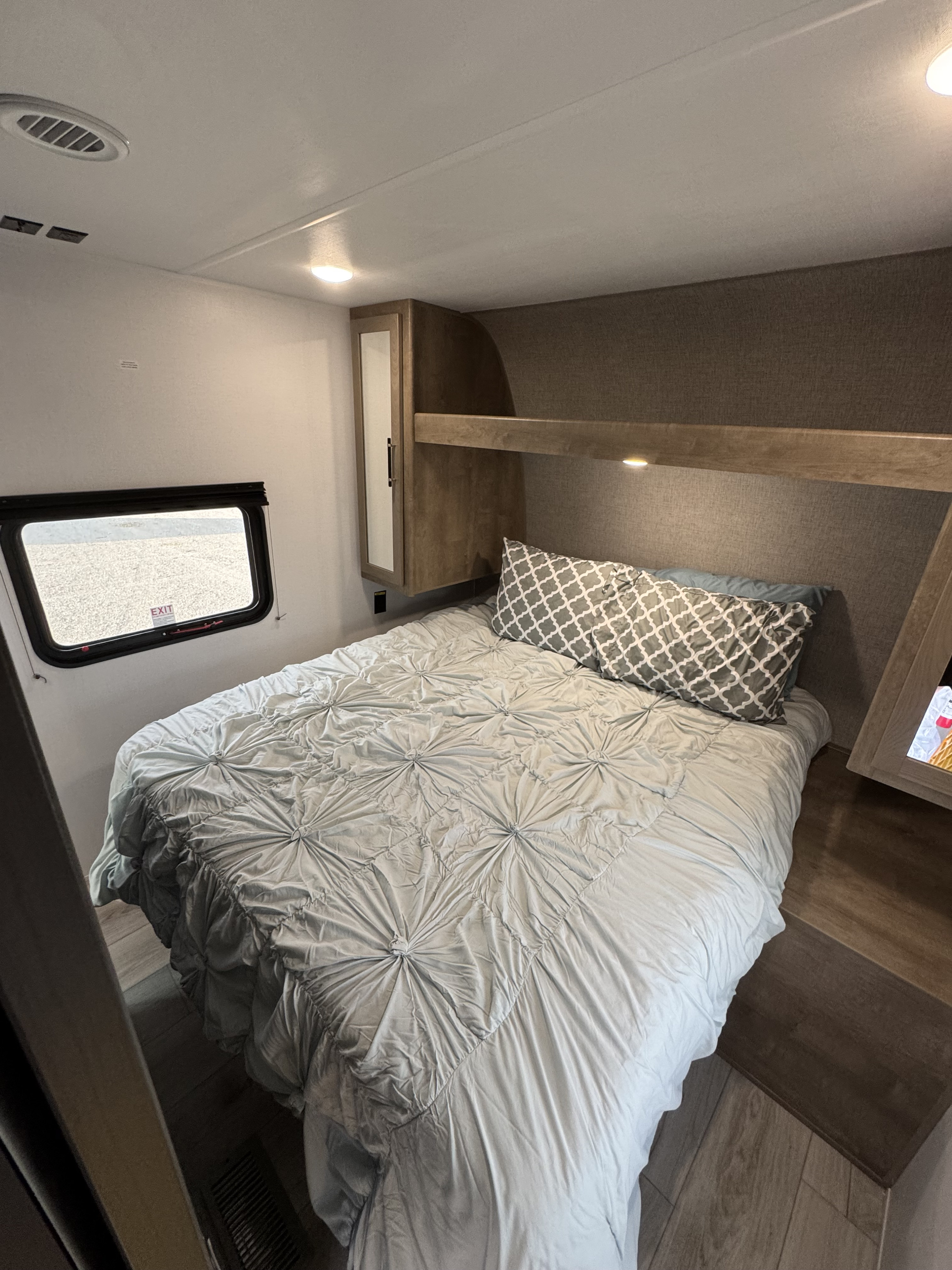 Cozy RV rental bedroom features a comfy bed with blue comforter, built-in storage, window, and wood-look flooring.. Keystone Springdale Classic 261BHC 2025
