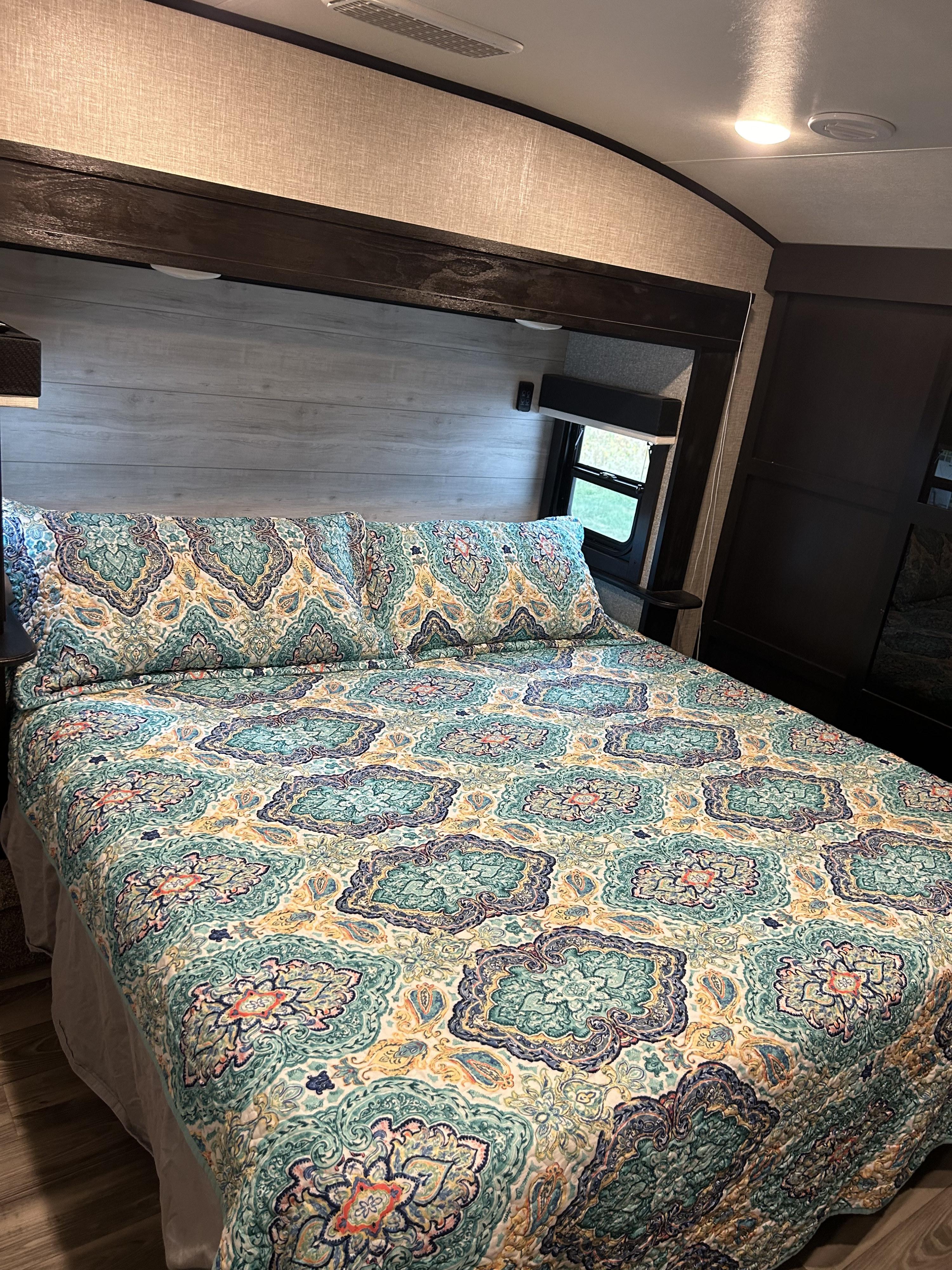 Cozy RV rental bedroom featuring a vibrant, patterned bed with matching pillows and a scenic window view.. Jayco Eagle 2023