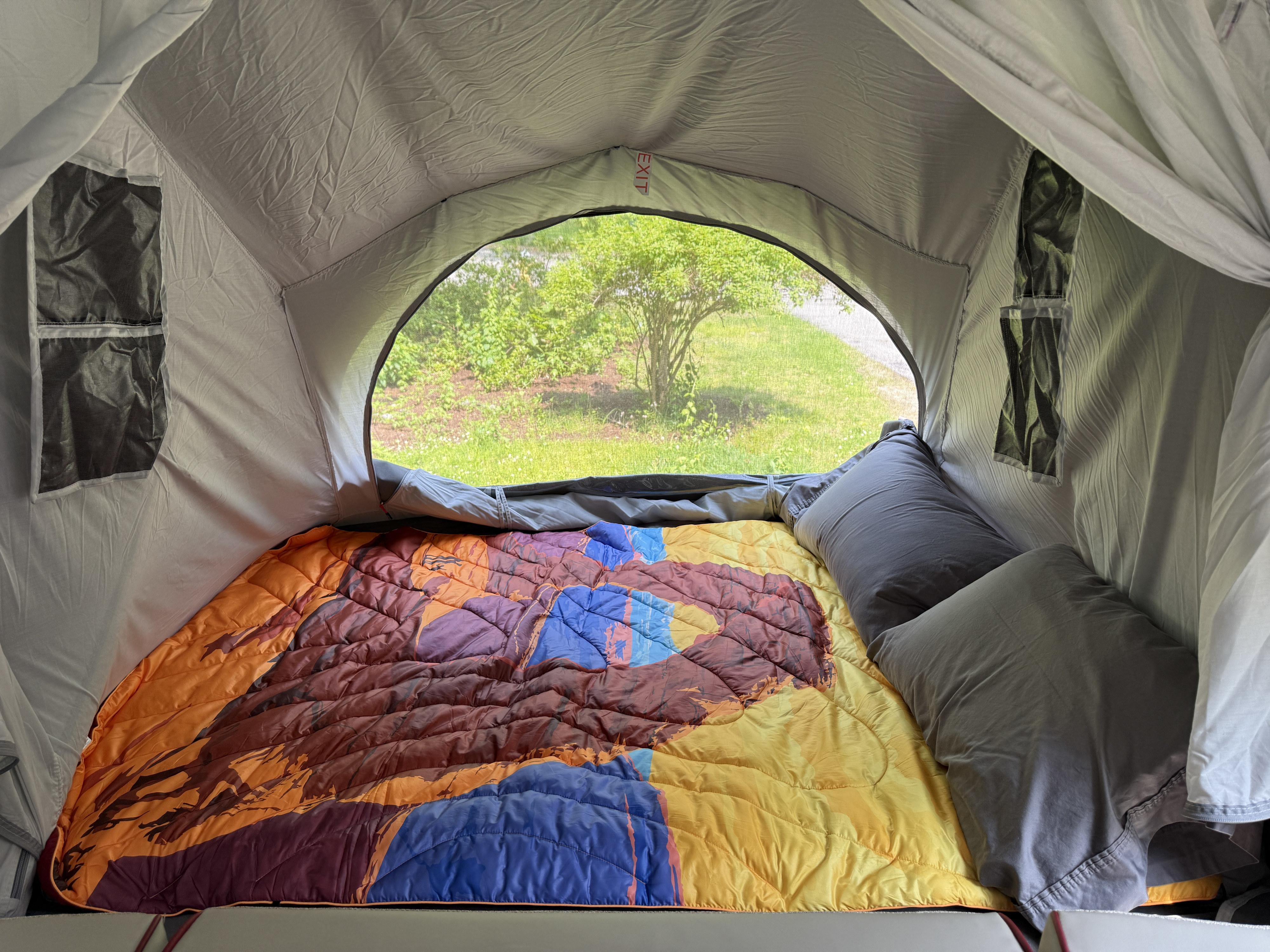 Cozy RV rental interior with a vibrant sleeping bag & tranquil outdoor view, perfect for camping comfort.. Opus Camper Opus Camper Popup Trailer 2023