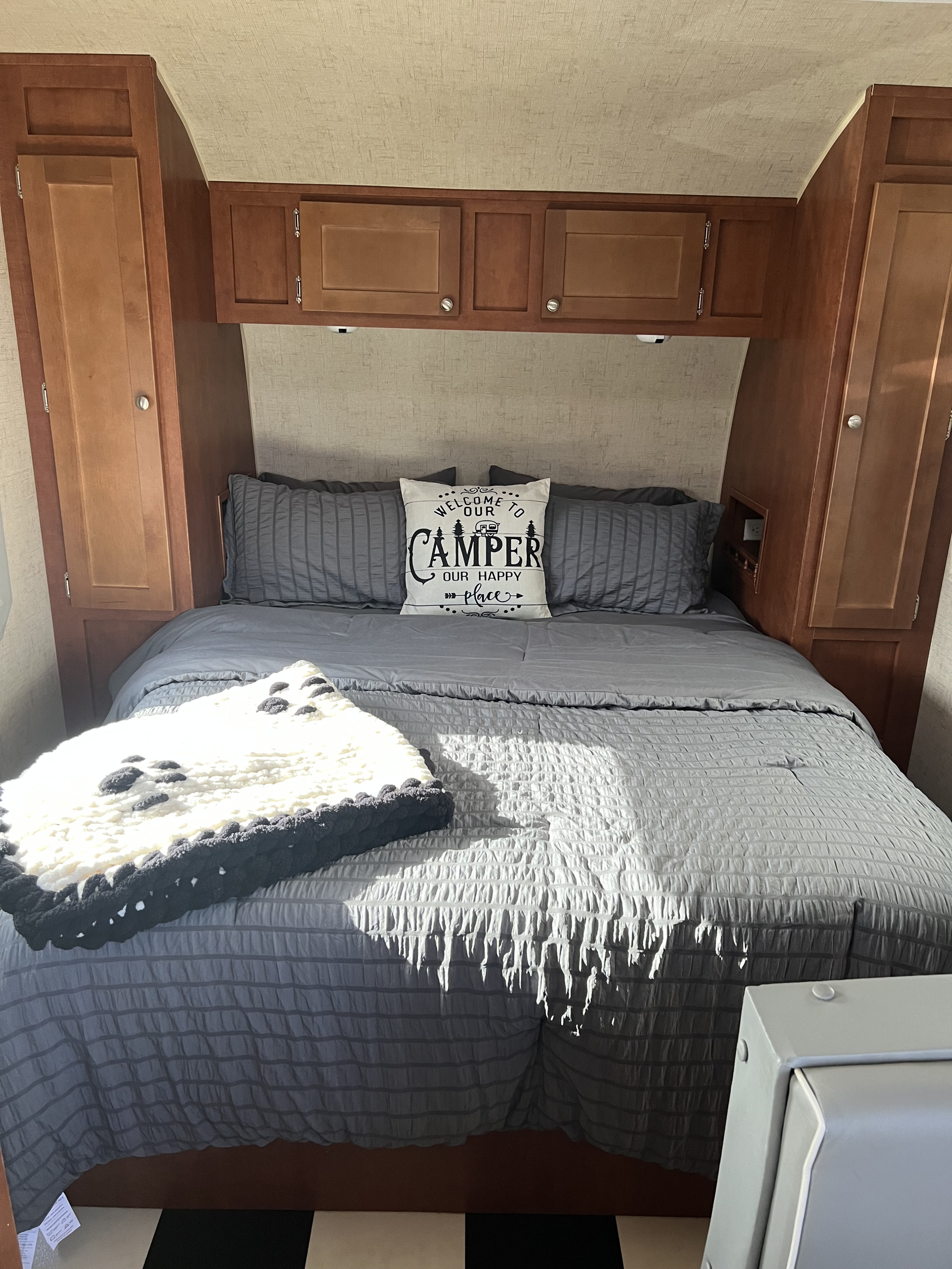 Cozy RV rental bedroom with gray bedding, a "camper" pillow, and wooden cabinets. Perfect for your next adventure!. Riverside Travel Trailer White Water Retro 2016