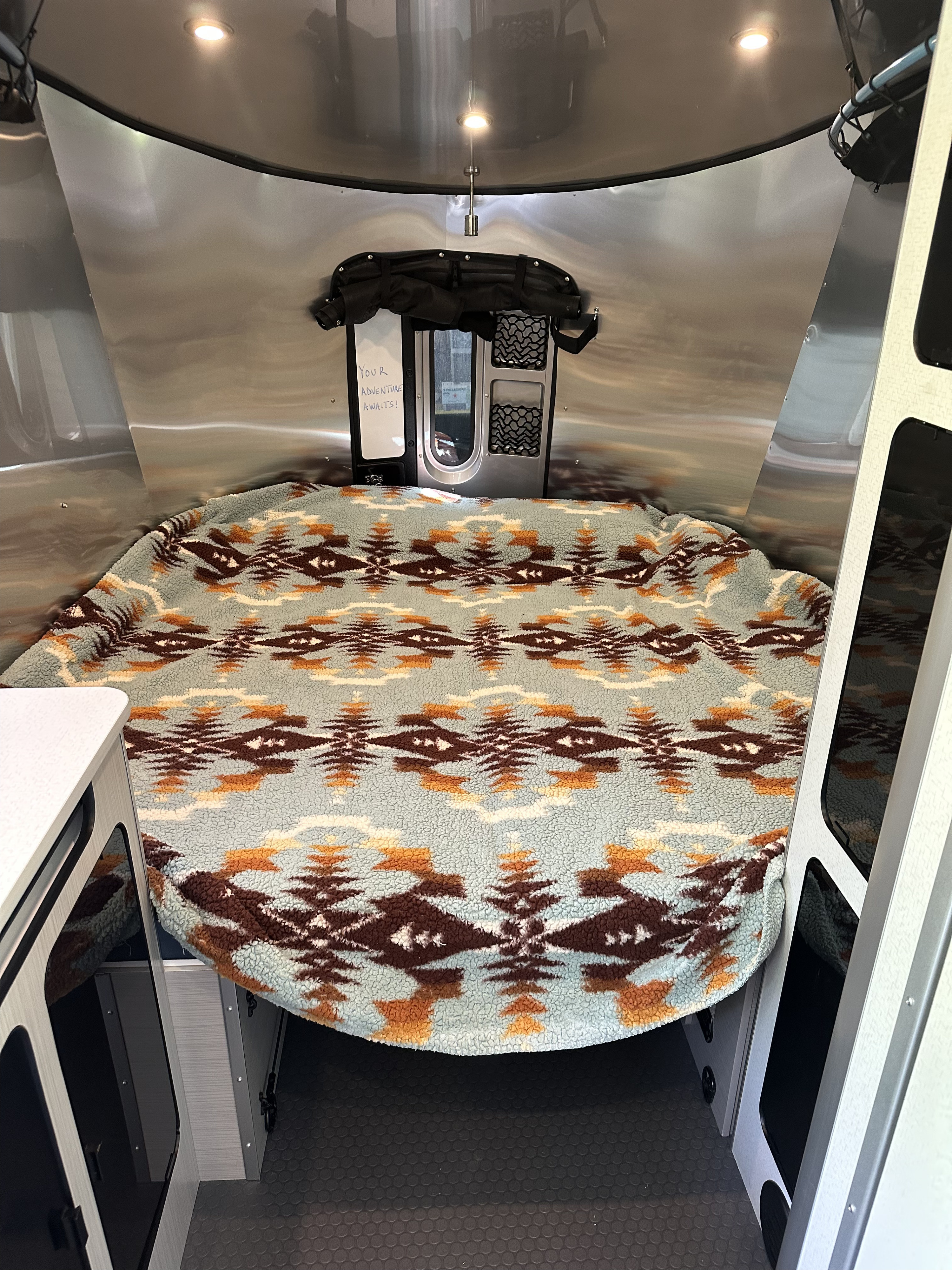 Inside a compact RV rental: a cozy bed with a Southwestern-style blanket and metallic walls. Your adventure awaits!. Airstream Basecamp 2024