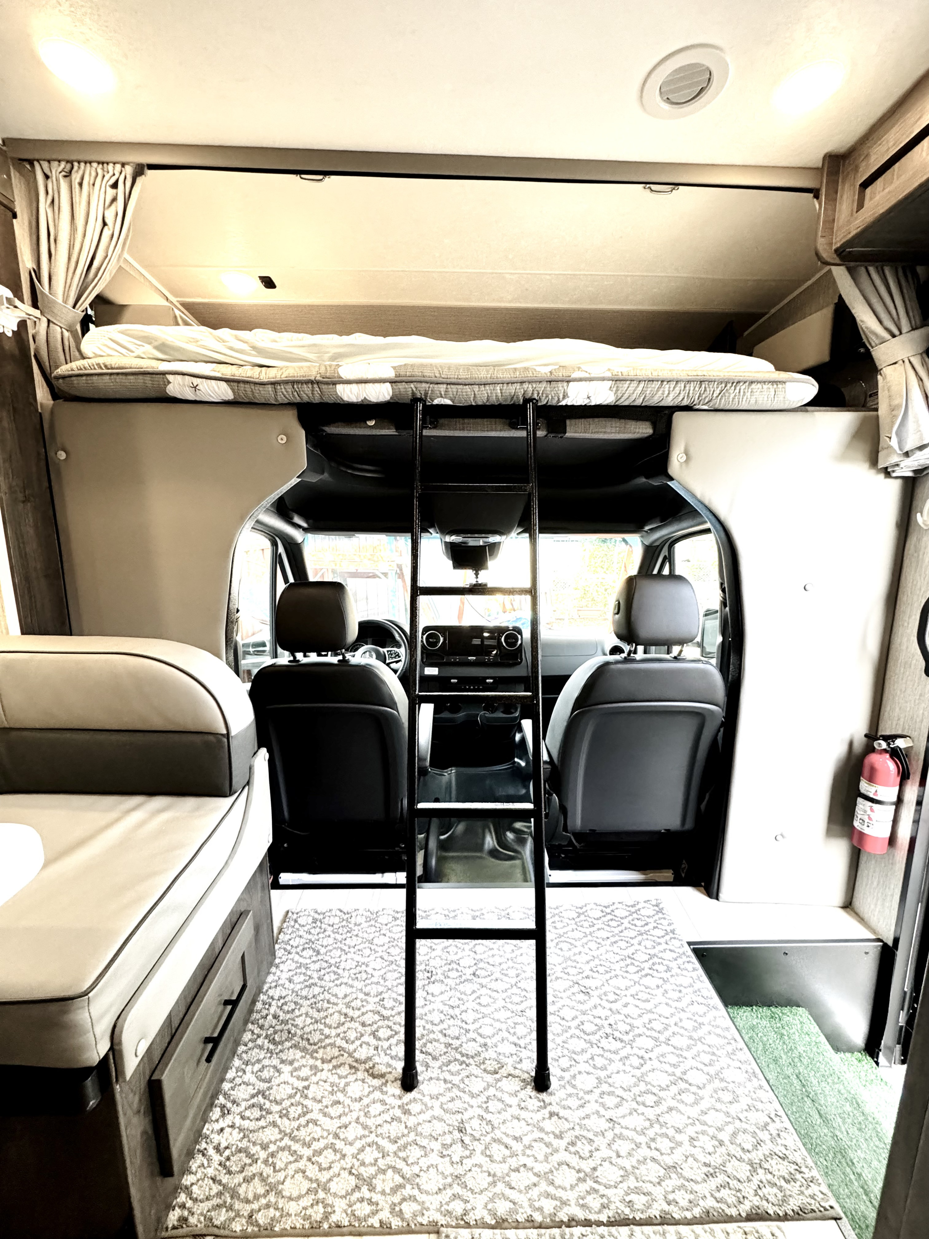 View of an RV rental's cleverly designed interior with an overhead bunk bed, ladder to the cab, and comfortable seating.. Forest River Coachmen Prism LE 2023