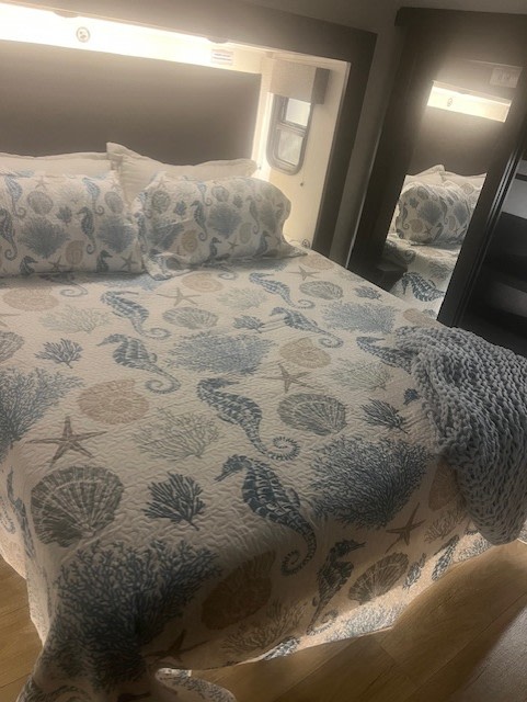 Inviting RV rental bedroom with a seahorse and seashell patterned bedspread and cozy throw blanket.. Forest River Sabre 2025
