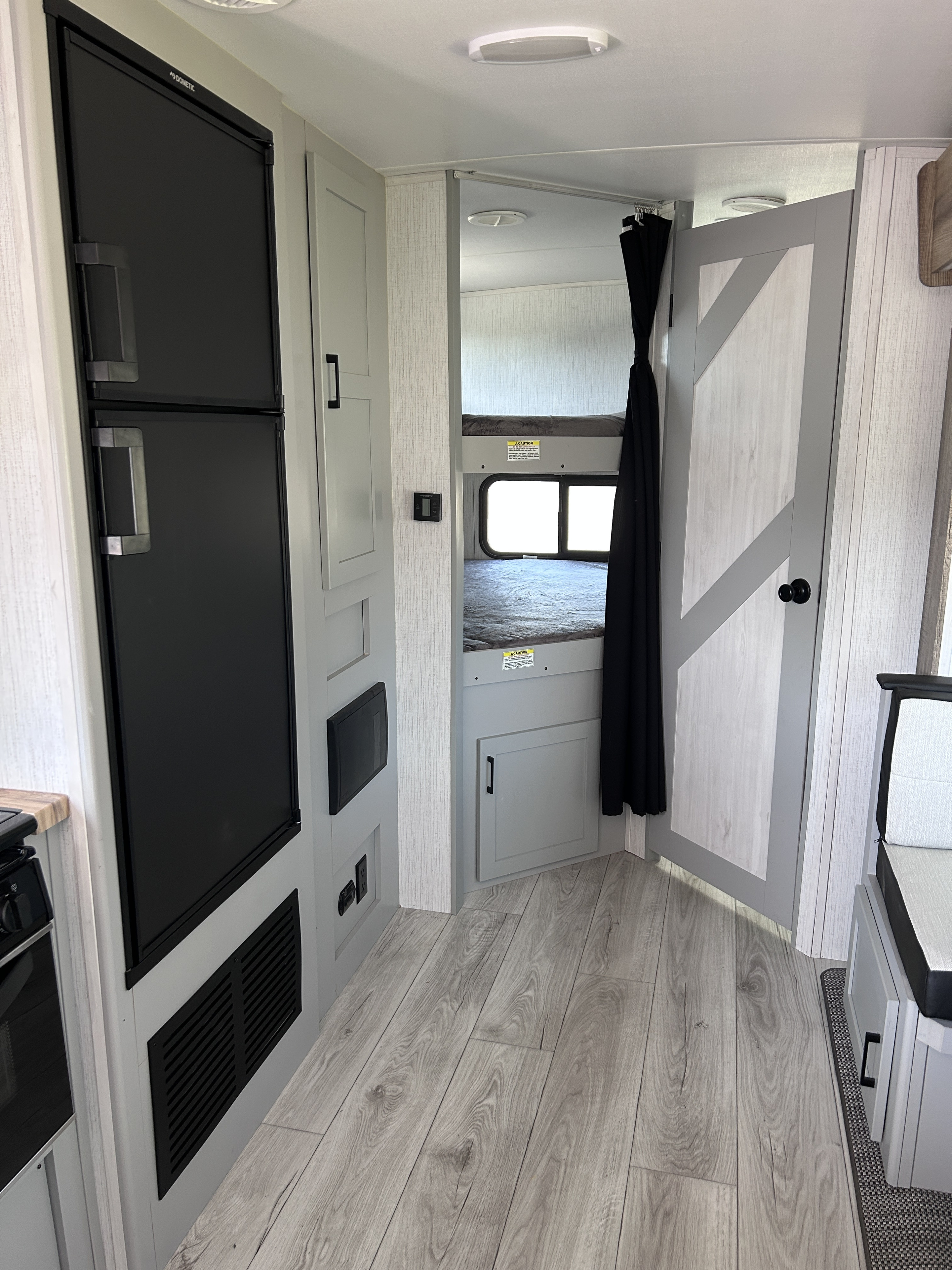Inside an RV rental: a black Dometic fridge, stacked bunk beds, and a light wood-look floor. Functional, compact living.. Heartland RVs North Trail 2023