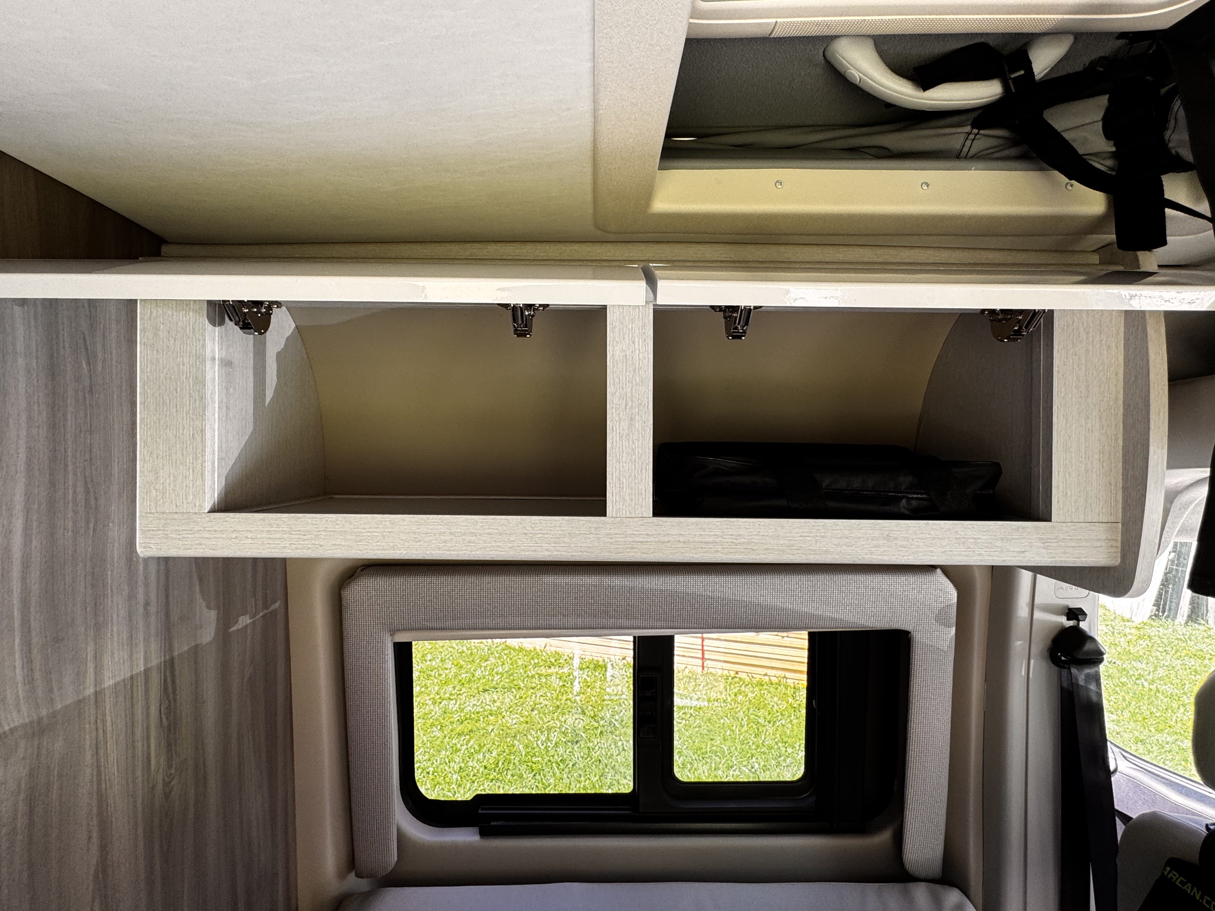 Spacious RV rental interior: overhead storage with open cabinets, a window views green grass.. Thor Tellaro 2023