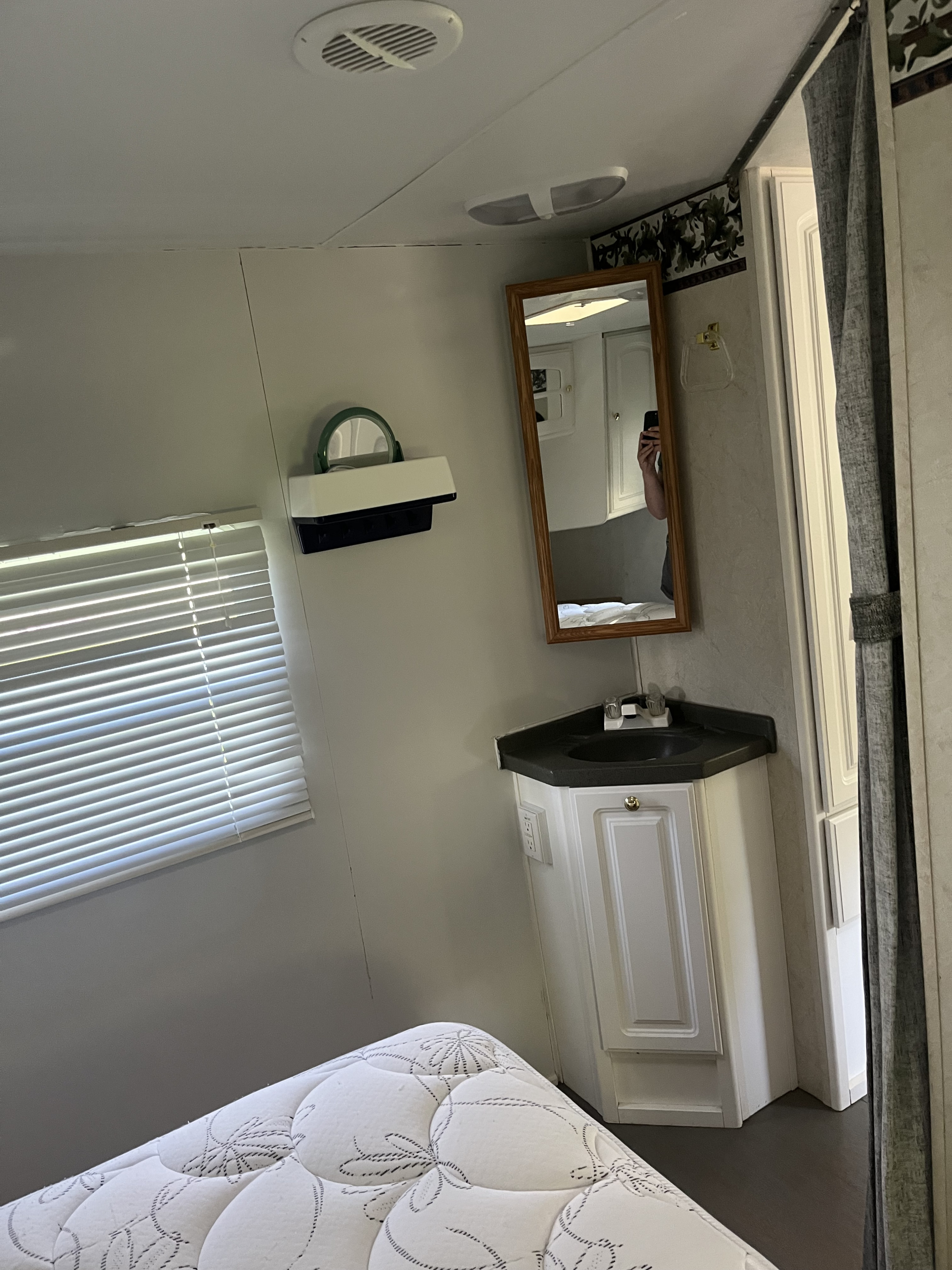 Inside an RV rental: a compact bedroom/bathroom area with a comfortable bed, corner sink vanity, and mirror.. Keystone RV LIteway Outback 2003