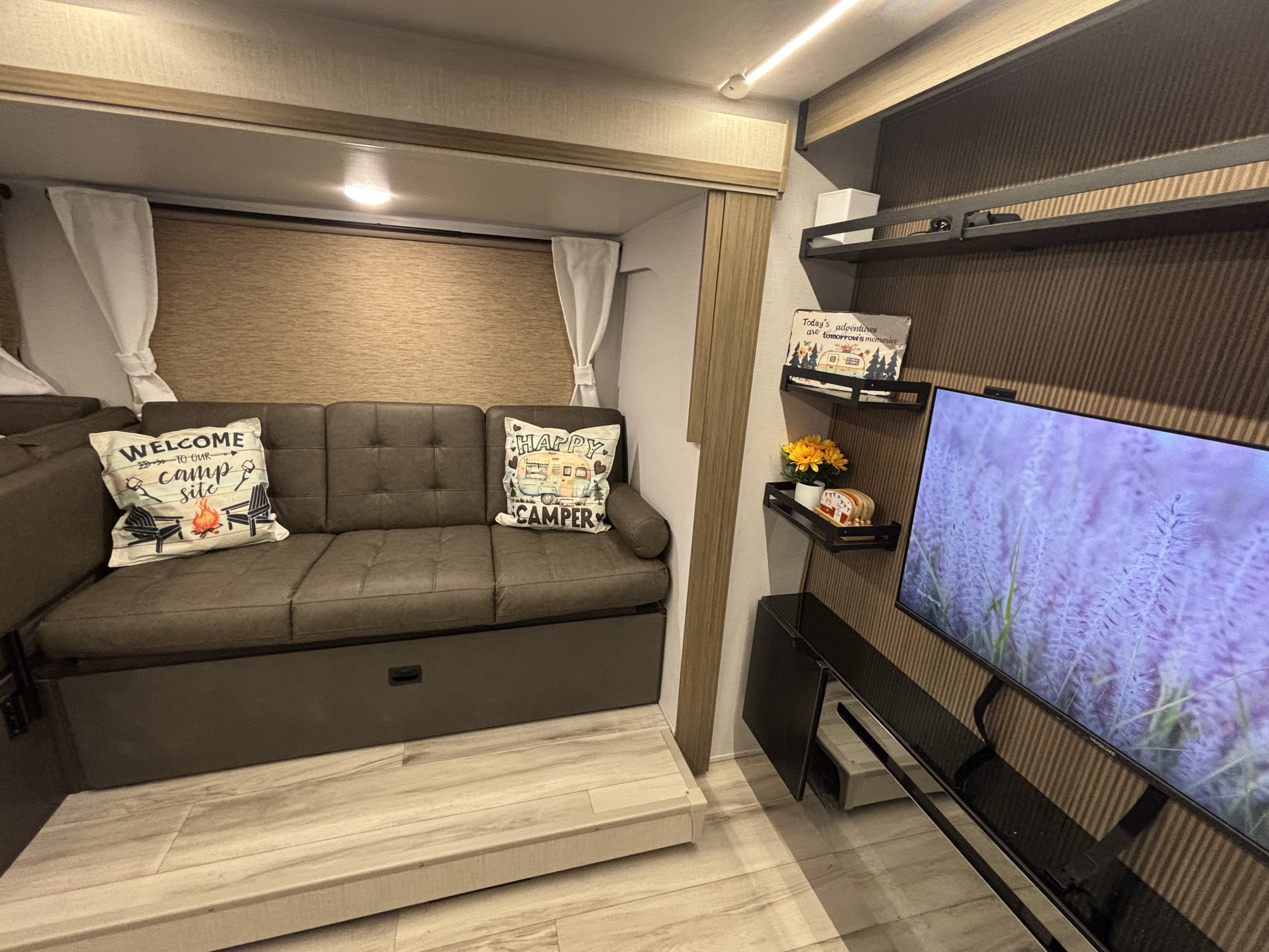Cozy RV rental living space with a comfy sofa, TV, and charming camp-themed decor.. Forest River Wildwood X-LITE 263BHXL 2025