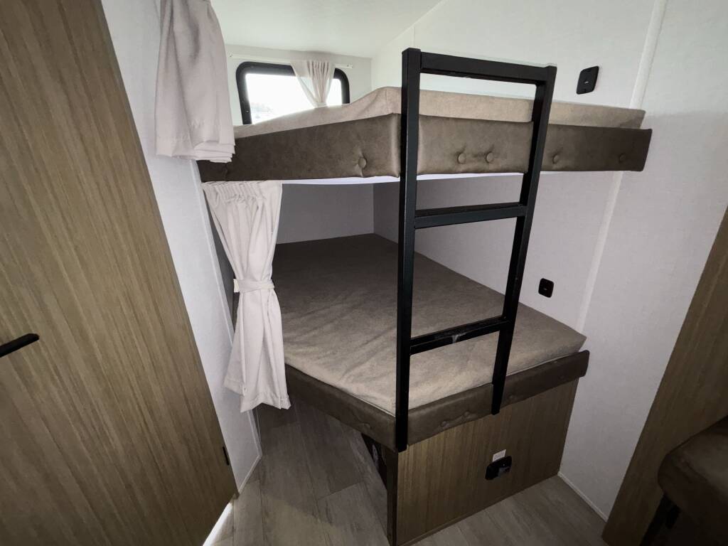 RV rental bunk beds with ladder and privacy curtains in a modern camper interior. Provides cozy sleeping.. Forest River Wildwood X-LITE 263BHXL 2025