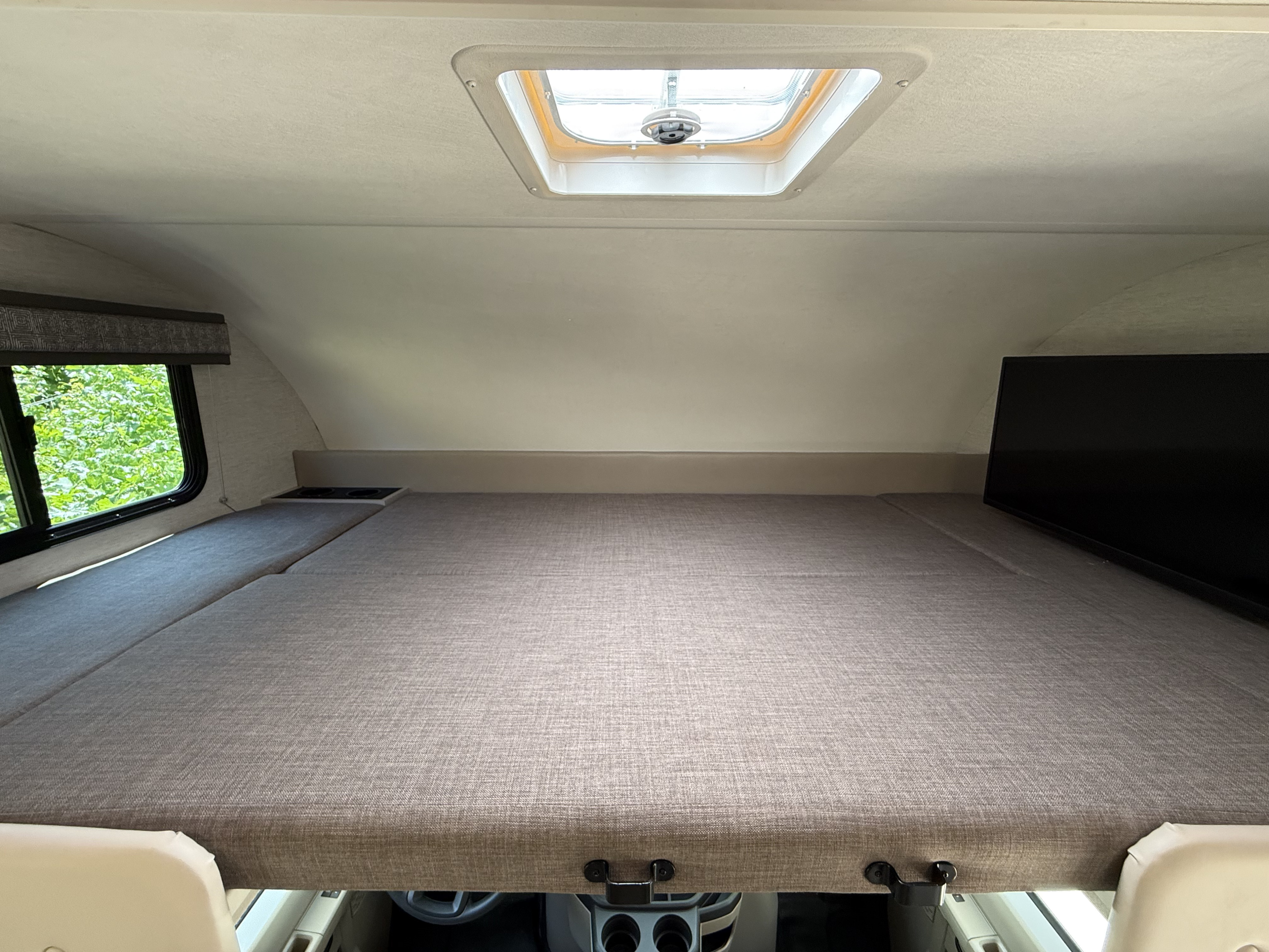 This image shows the comfortable cab-over bunk in an RV rental, complete with a bed, window, skylight, and TV.. Thor Chateau 2025