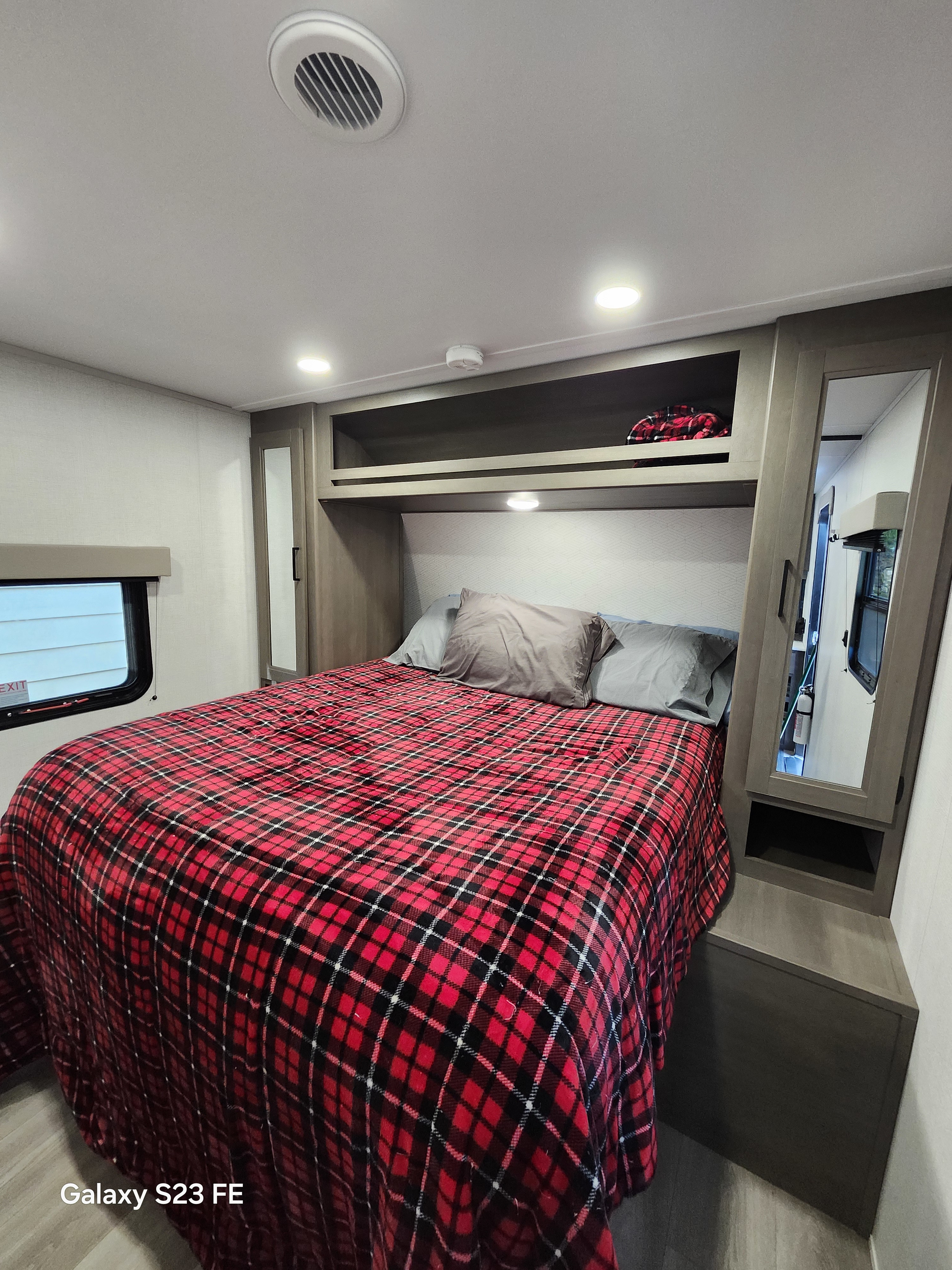 Cozy RV rental bedroom with a red plaid blanket, built-in storage, and modern lighting. Ideal for travel.. Grand Design Transcend 2025