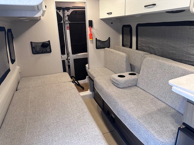This RV rental offers a versatile interior with light gray convertible beds, sofa seating, and overhead storage.. Thor Dazzle 2024