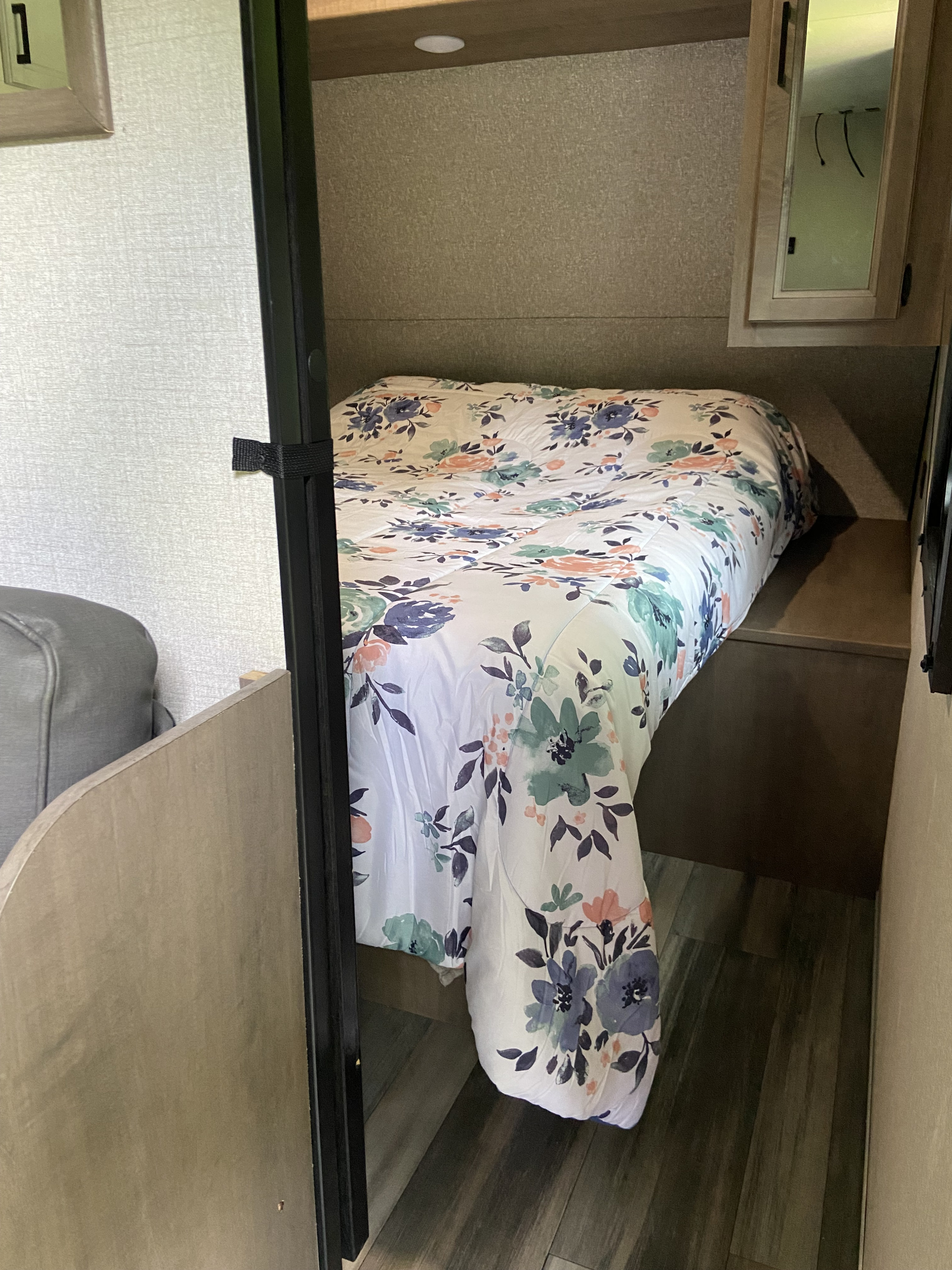 An RV rental bedroom featuring a bed with a floral comforter, compact layout, side shelf, and overhead mirrored cabinet.. Highland Ridge RV Open Range 2020