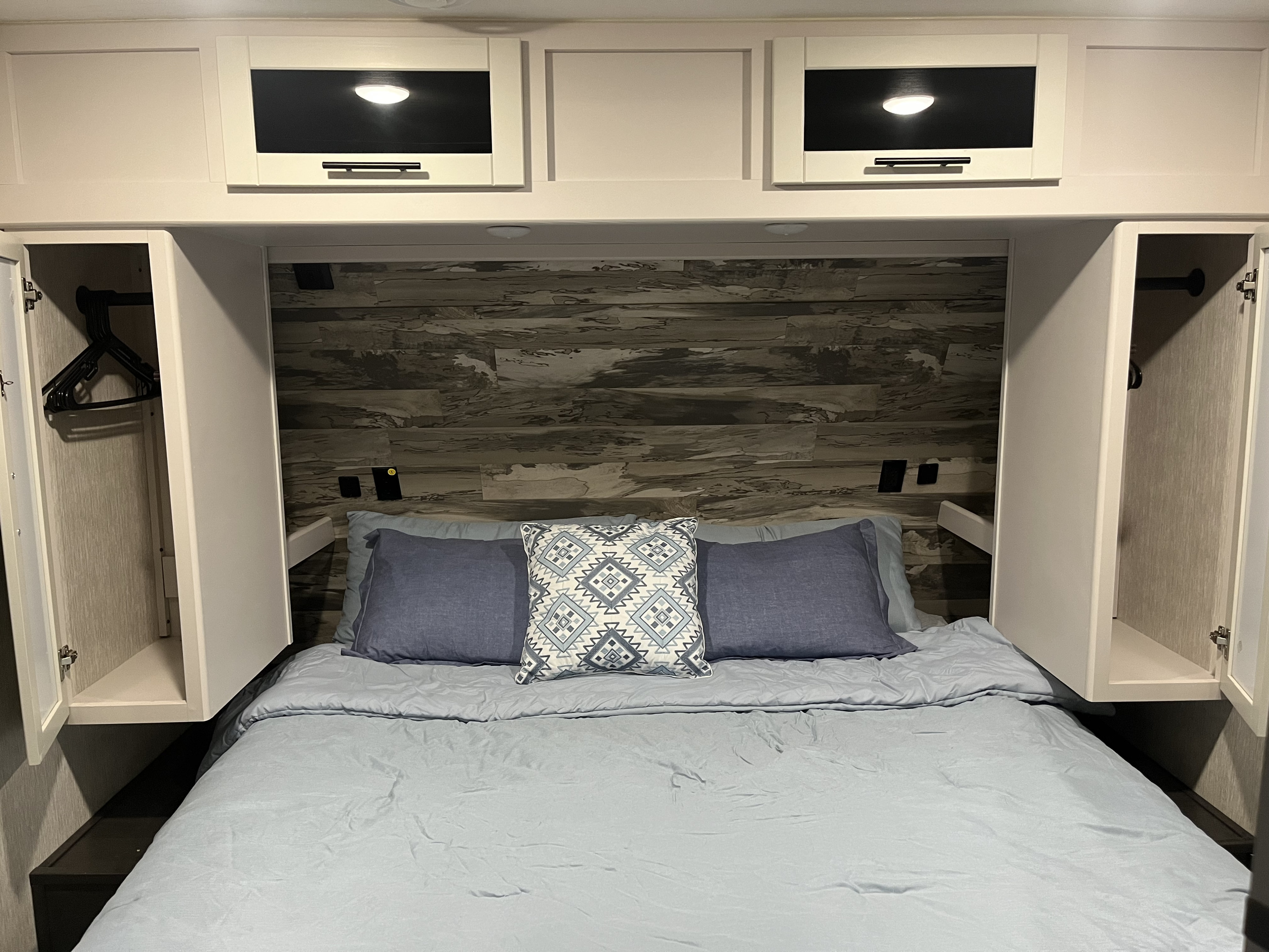 Cozy RV rental bedroom featuring a light blue bed, patterned pillow, wood-look headboard, and functional overhead storage.. Crossroads RV Cruiser Aire 2022