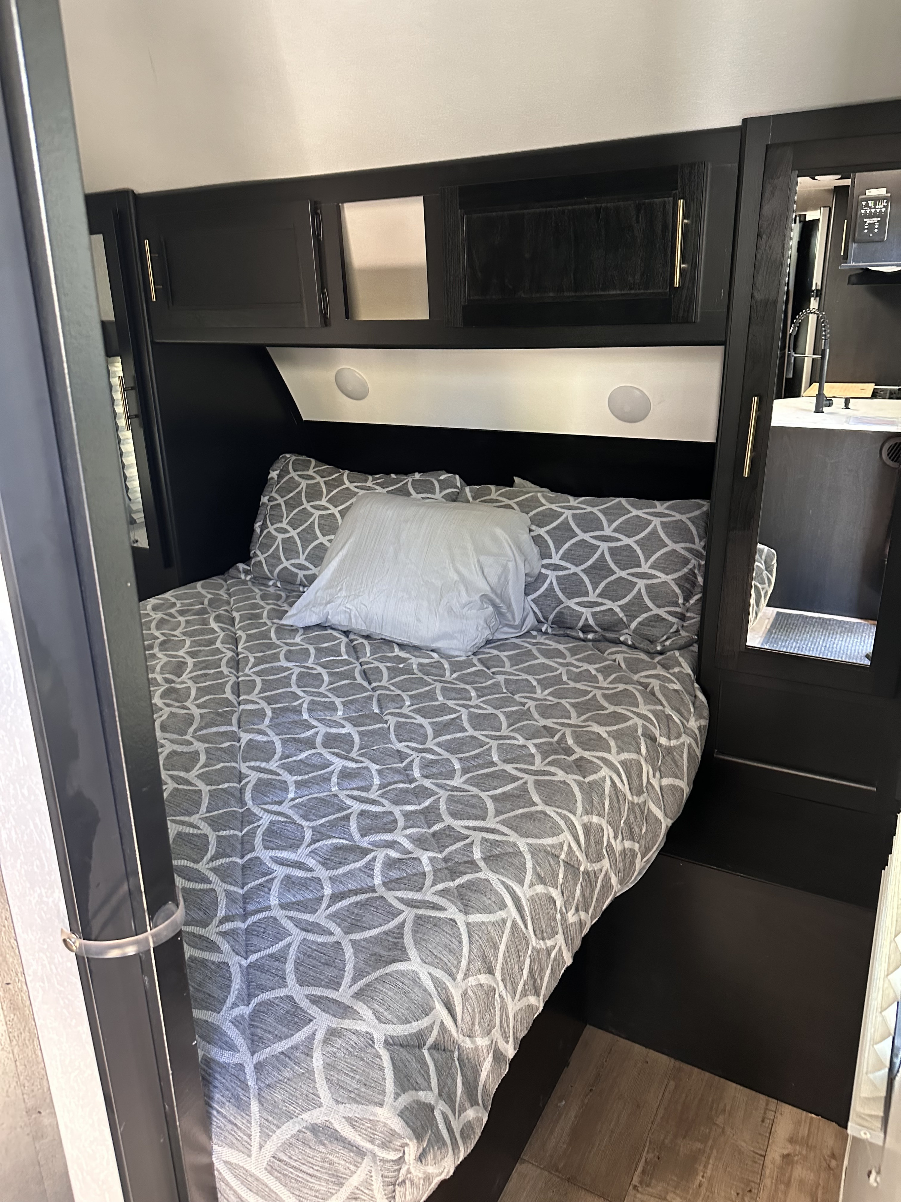 This image shows a modern RV rental bedroom with dark cabinetry, a bed with gray patterned bedding, and integrated lighting.. Forest River Cherokee 2022