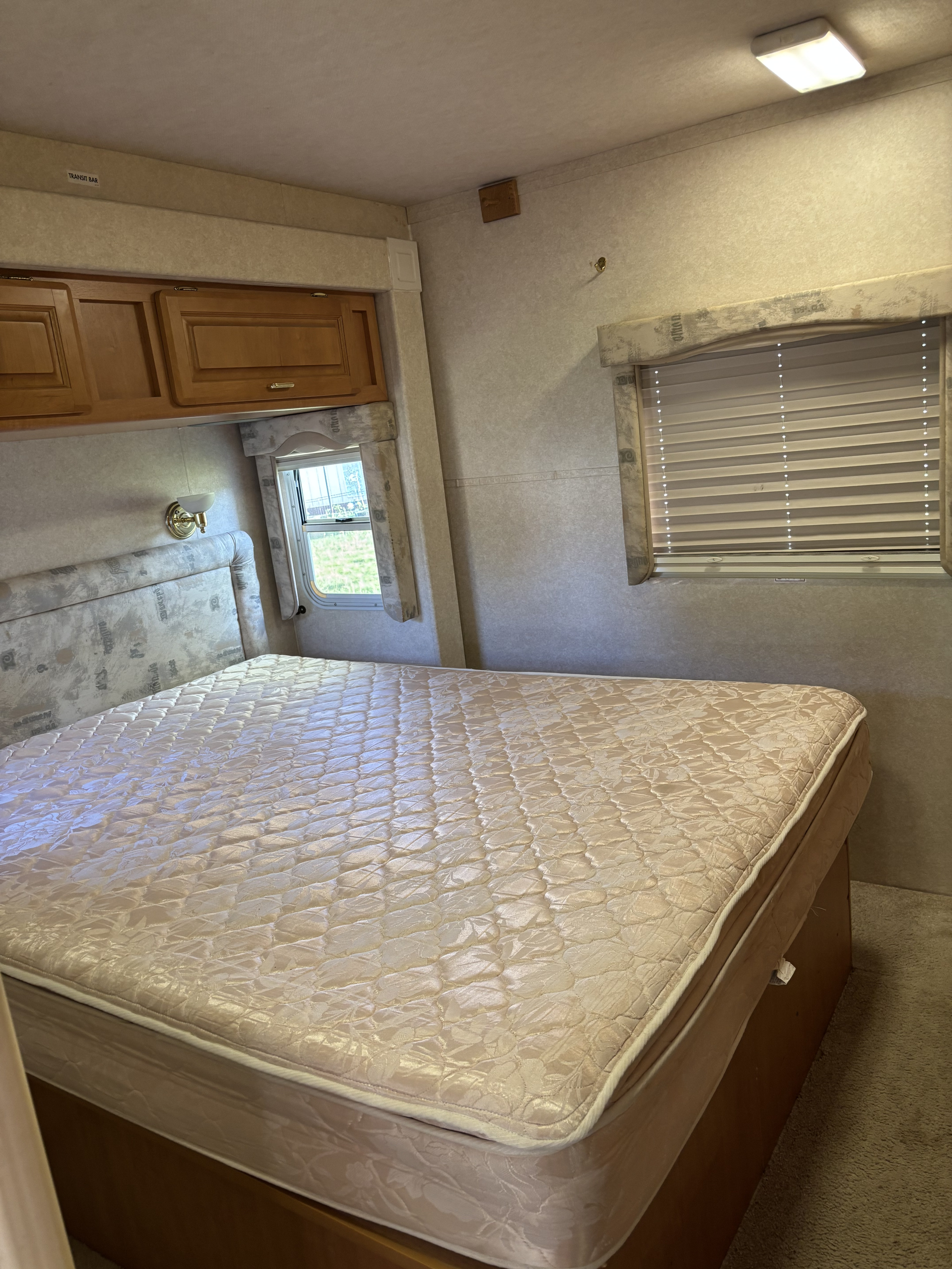 Clean RV rental bedroom with a large mattress, upholstered headboard, wooden overhead cabinets, and two windows with blinds.. Jayco Granite Ridge 2002