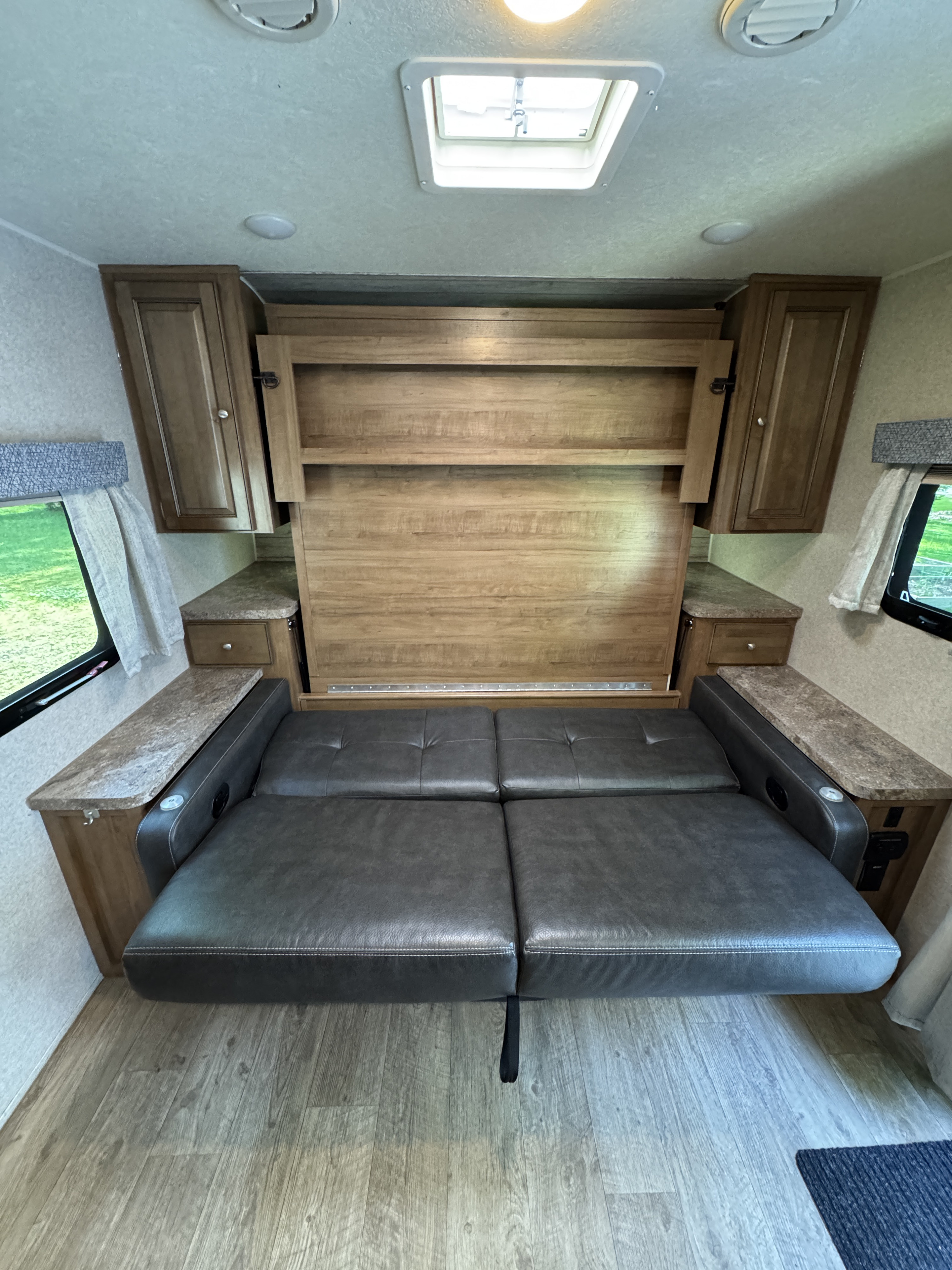 Modern RV rental interior with a versatile grey sofa that converts to a bed, surrounded by storage and windows.. Forest River Rockwood Mini Lite 2019