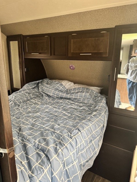 Comfortable RV rental bedroom. Features a large bed with blue patterned comforter and dark wood storage cabinets.. Forest River Cherokee Grey Wolf 2016