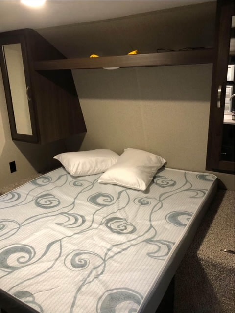 RV rental bed: a cozy sleeping area featuring a patterned mattress, two pillows, and practical overhead storage cabinetry.. Keystone RV Springdale 2020