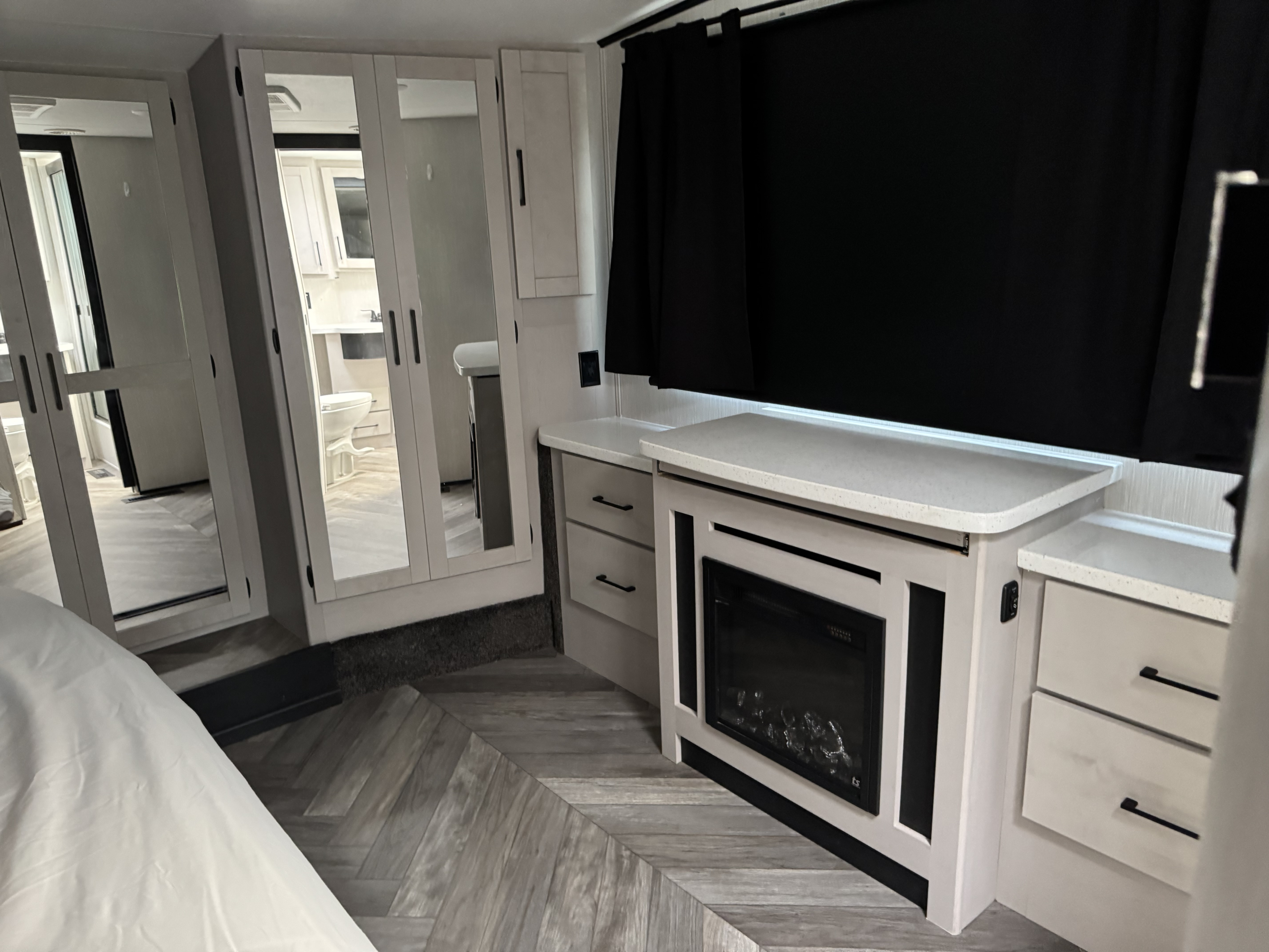 Cozy RV rental bedroom with mirrored closet, electric fireplace, and modern decor. Bathroom visible in reflection.. Heartland Toyhauler 2022