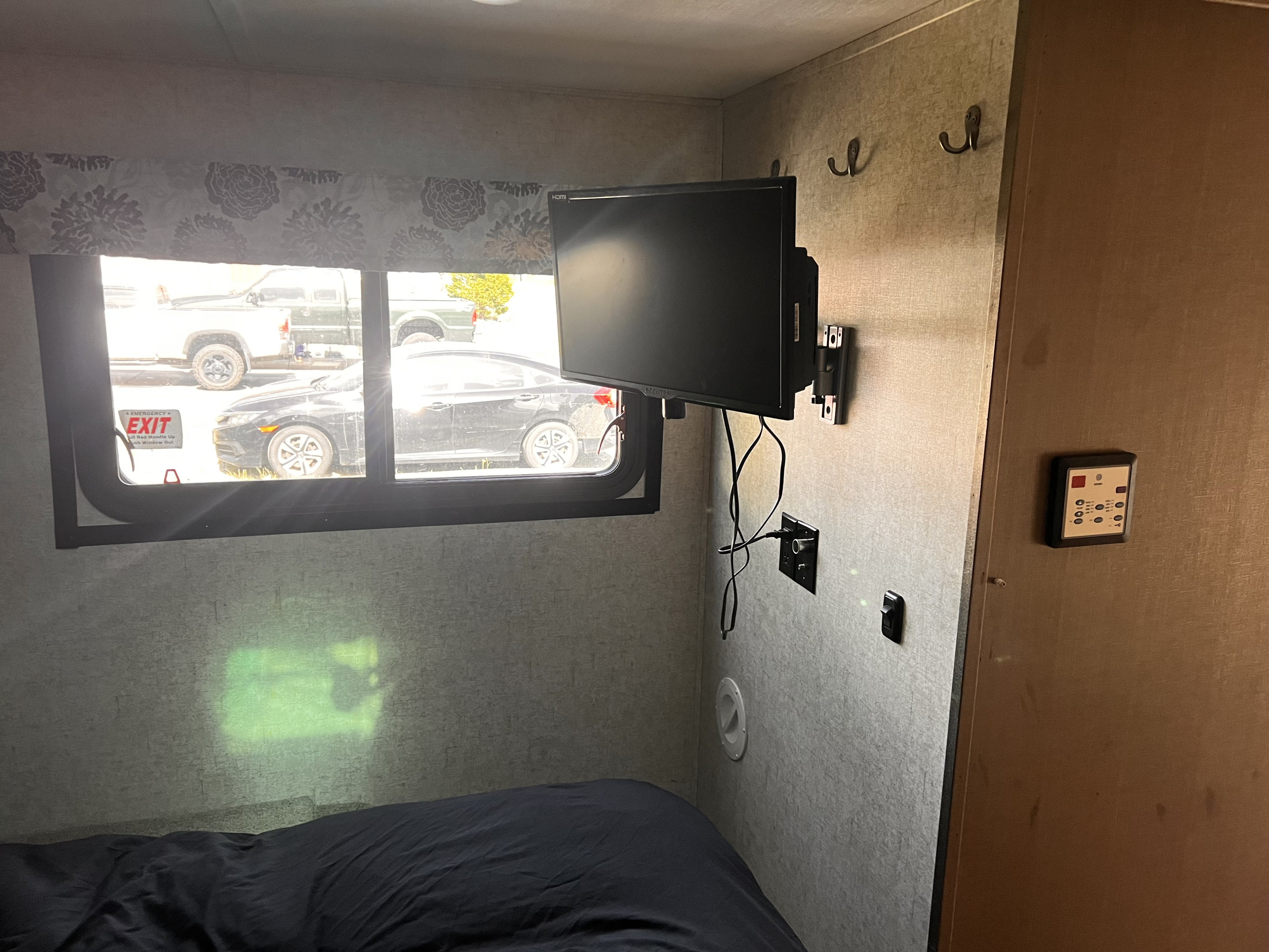 Inside an RV rental: a bedroom with an emergency exit window showing vehicles, a wall-mounted TV, and control panel.. Forester Forester Motorhome 2020