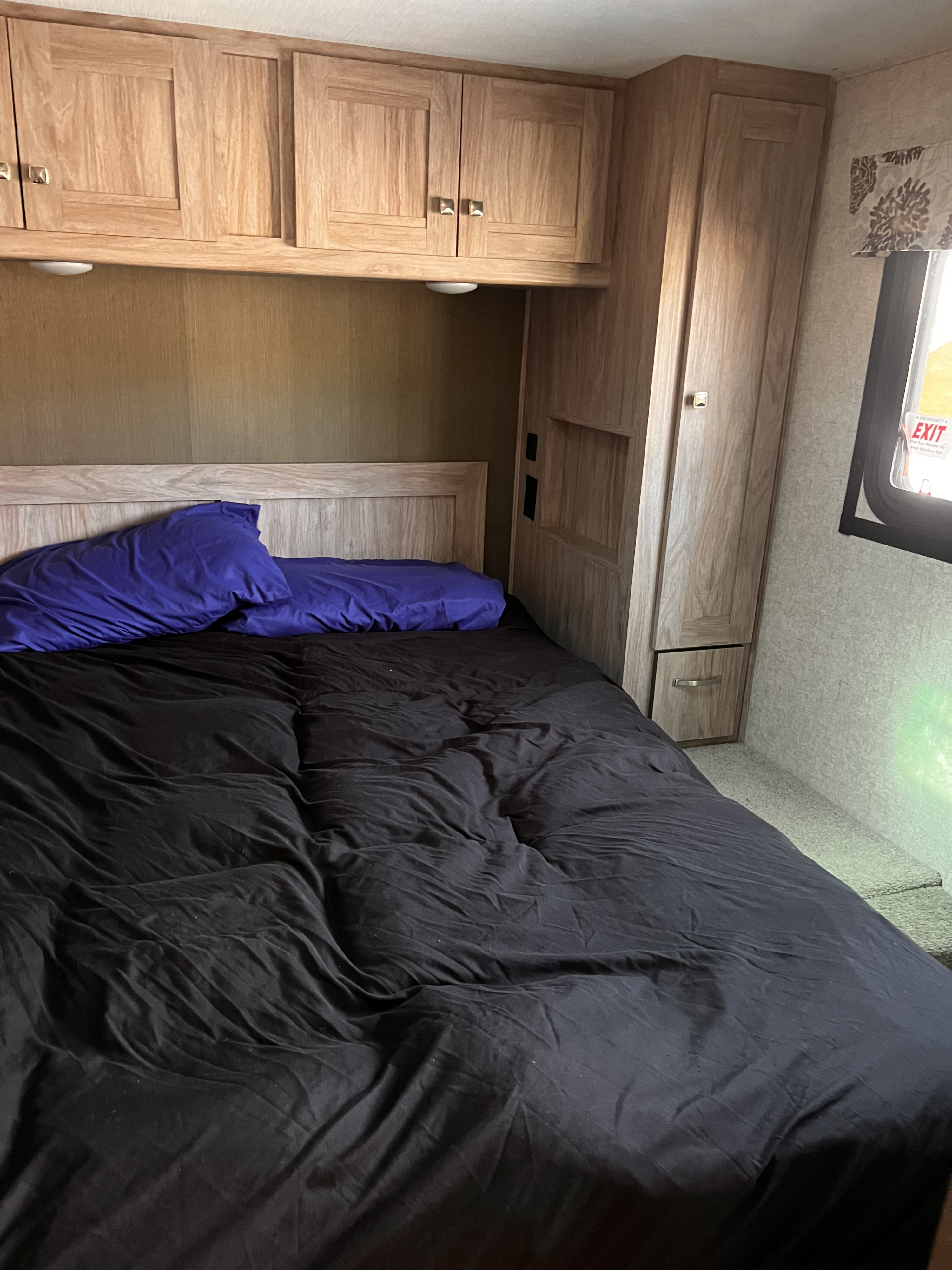 A comfortable RV rental bedroom featuring wood cabinets, a full-size bed with purple pillows, and a wardrobe.. Forester Forester Motorhome 2020