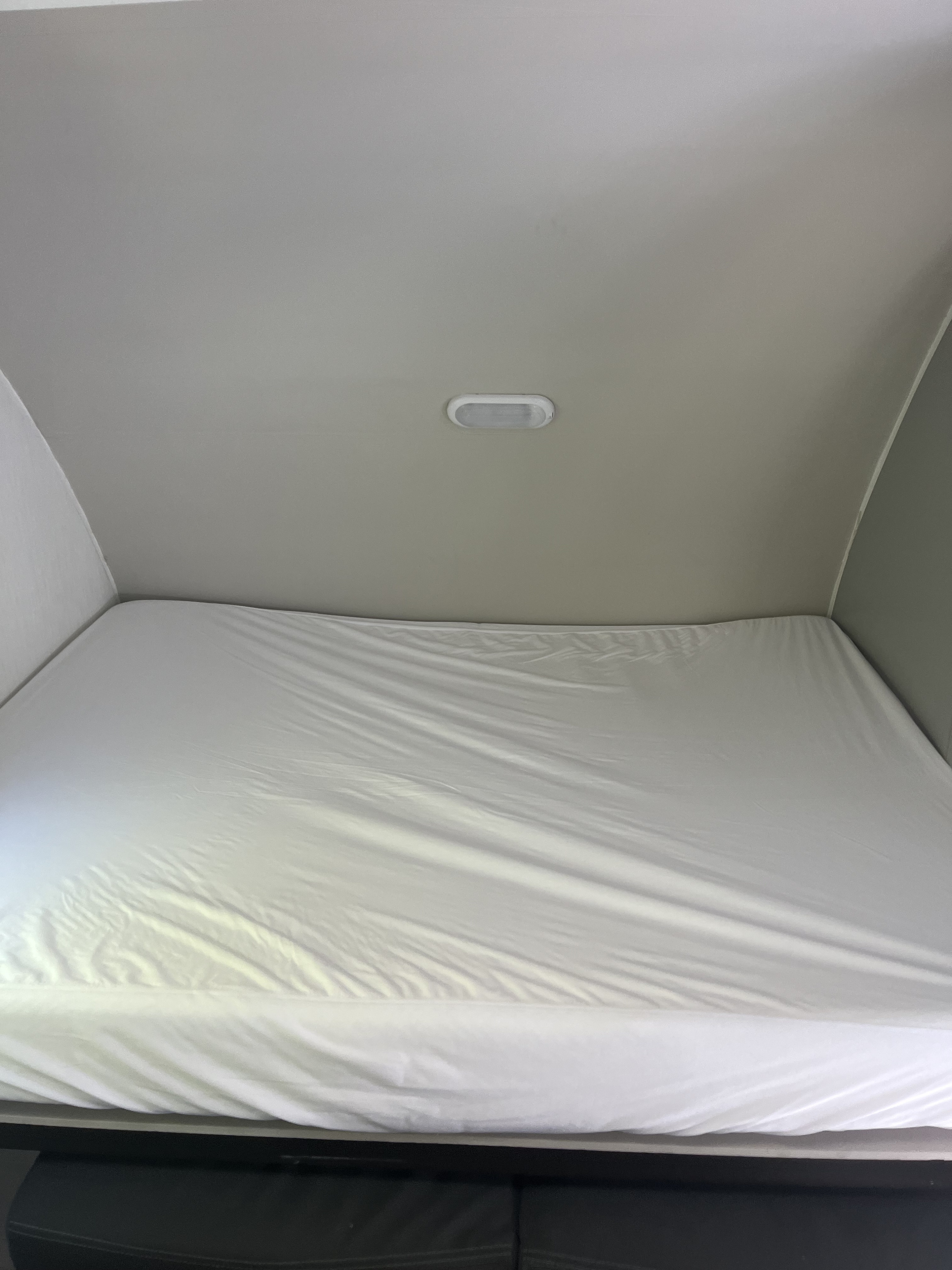 A compact RV rental sleeping area features a bed with white sheets and an overhead light, ready for a comfortable stay.. Forest River Vibe 2022