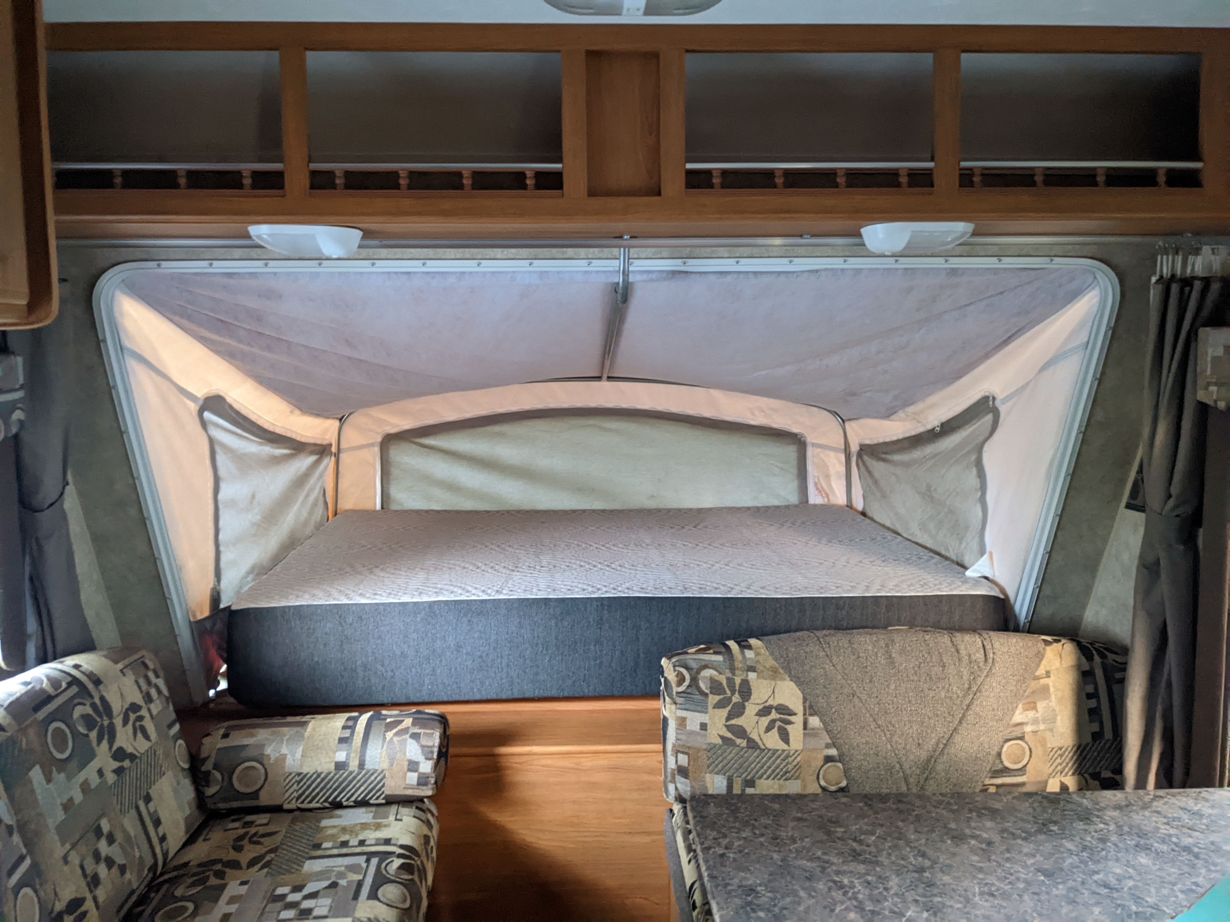 Interior of an RV rental pop-up camper showing a large bed, cozy seating, and overhead storage cabinets.. Forest River Surveyor 2008