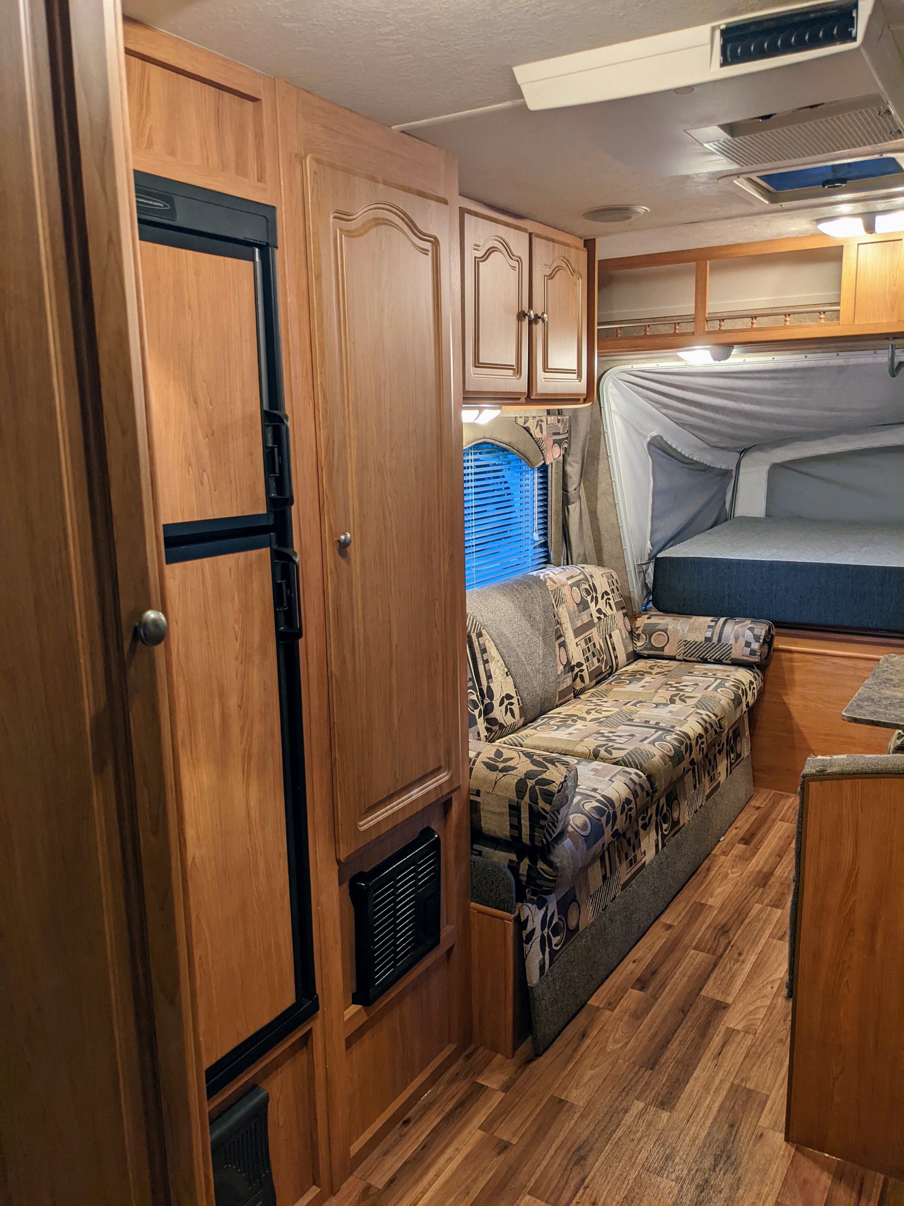 Step inside this cozy RV rental, featuring wood cabinetry, a patterned sofa, and a spacious bed in the rear pop-out section.. Forest River Surveyor 2008
