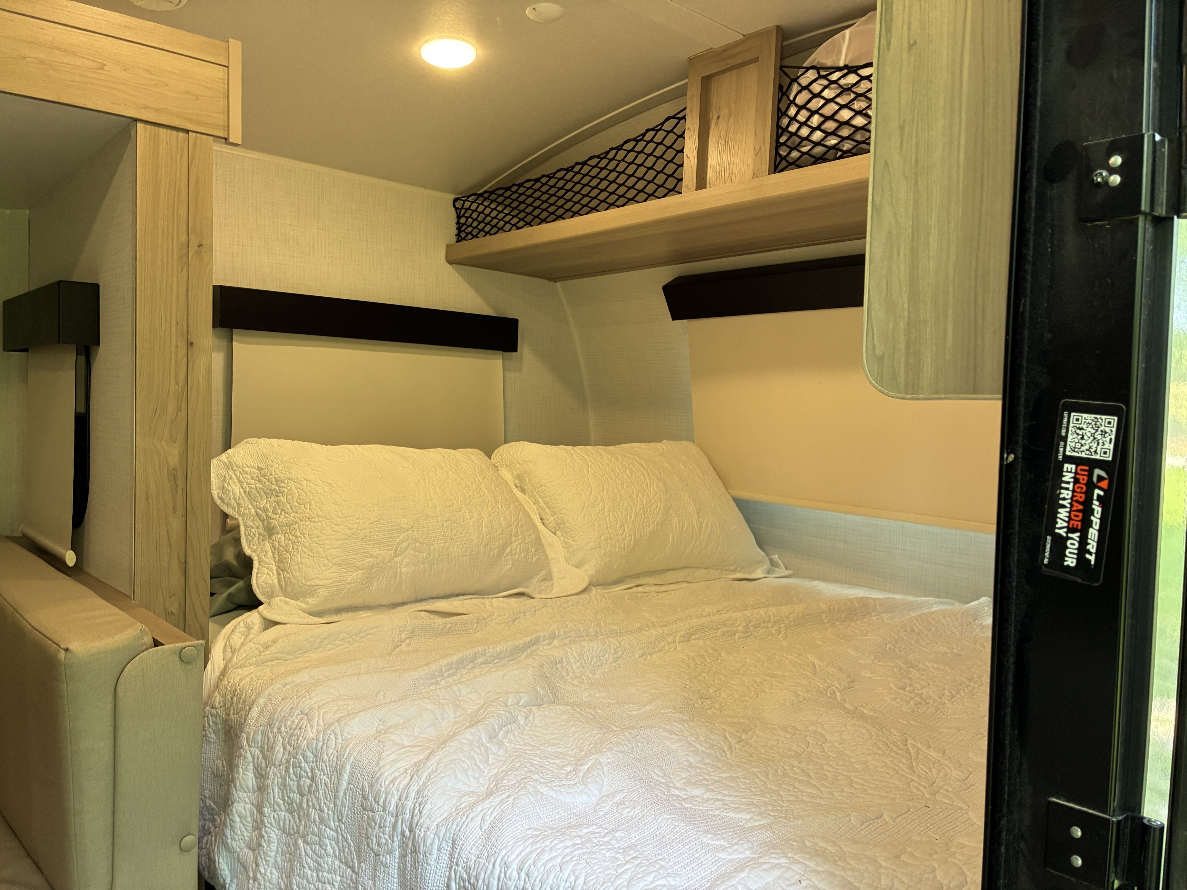 Compact RV rental bedroom with a cozy bed, white quilted bedding, padded headboard, and overhead net storage.. Forest River Rockwood Geo Pro 2024