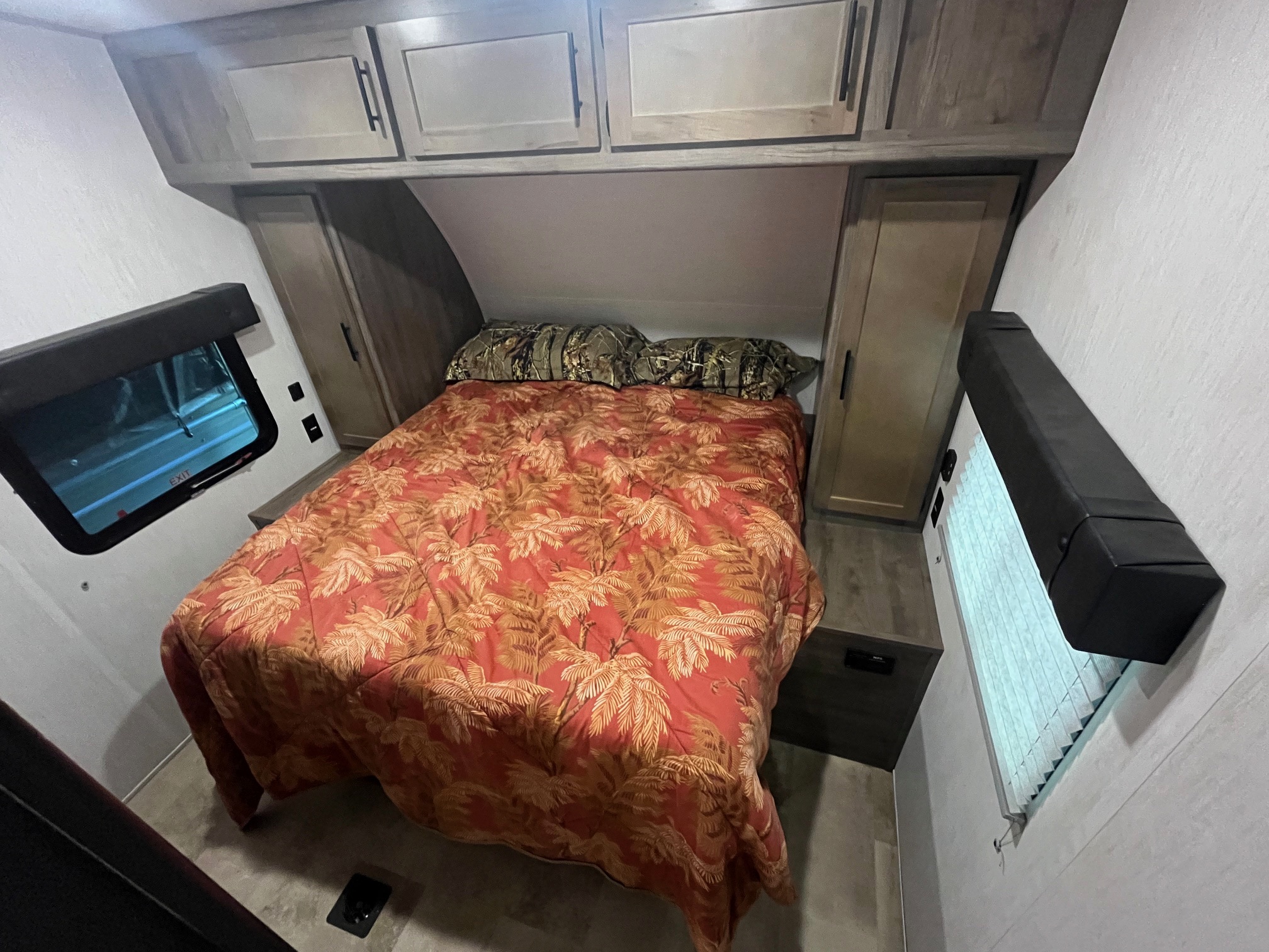 Inside an RV rental: a compact bedroom with a vibrant red palm-patterned comforter, camo pillows, and storage. Ideal for road trips.. Forest River Vengeance 2021